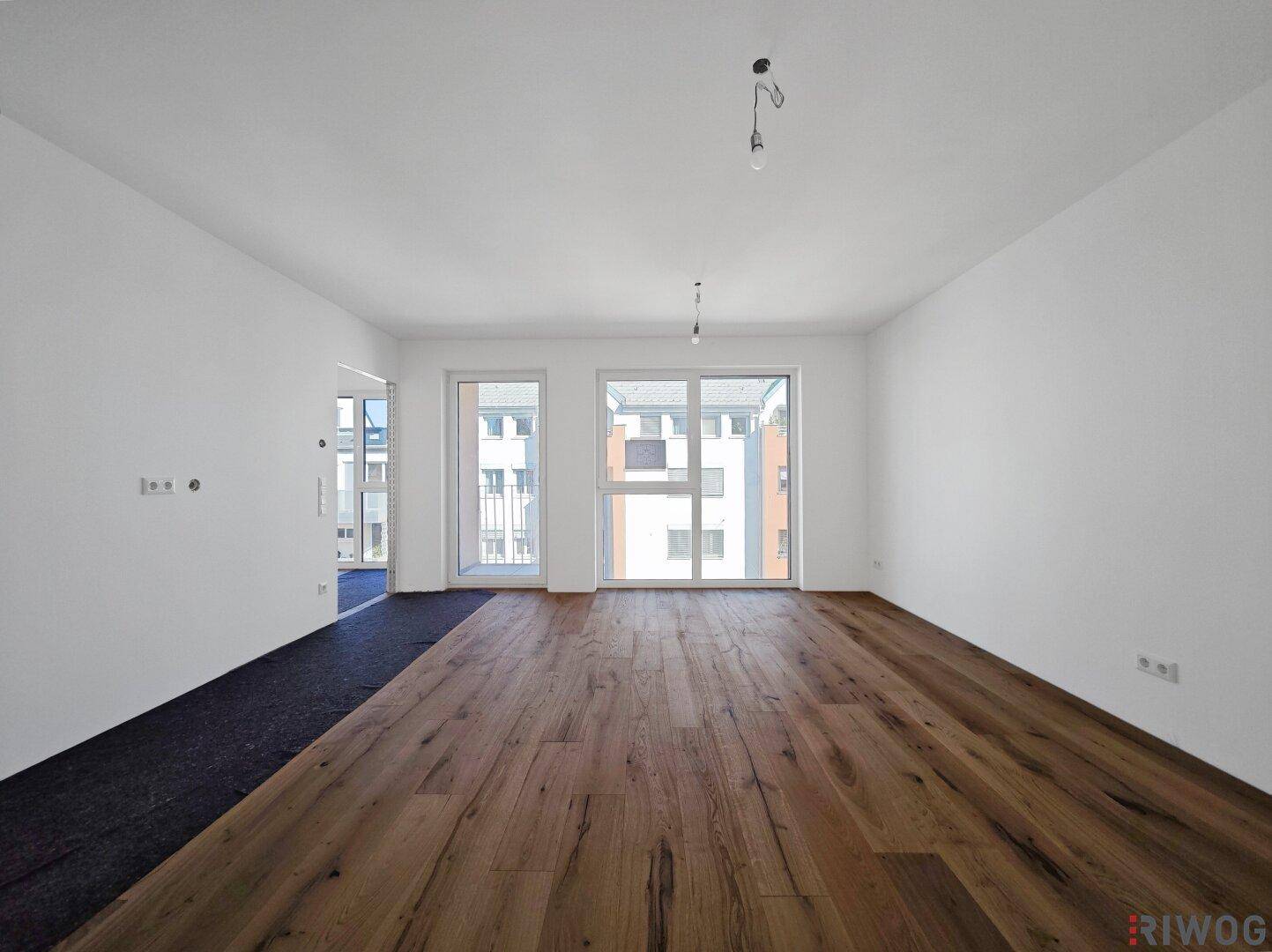 Lichtdurchfluteter Raum mit hochwertigem Holzparkett und Blick auf die umliegenden Gebäude.