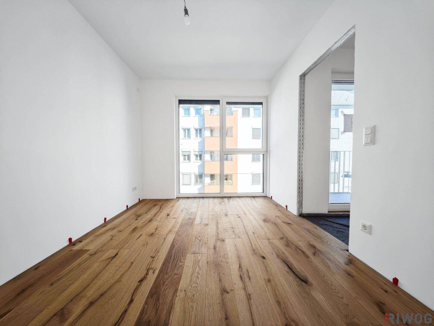 Helles Schlafzimmer mit neuem Holzfußboden und großem Fenster, bereit für die Fertigstellung.