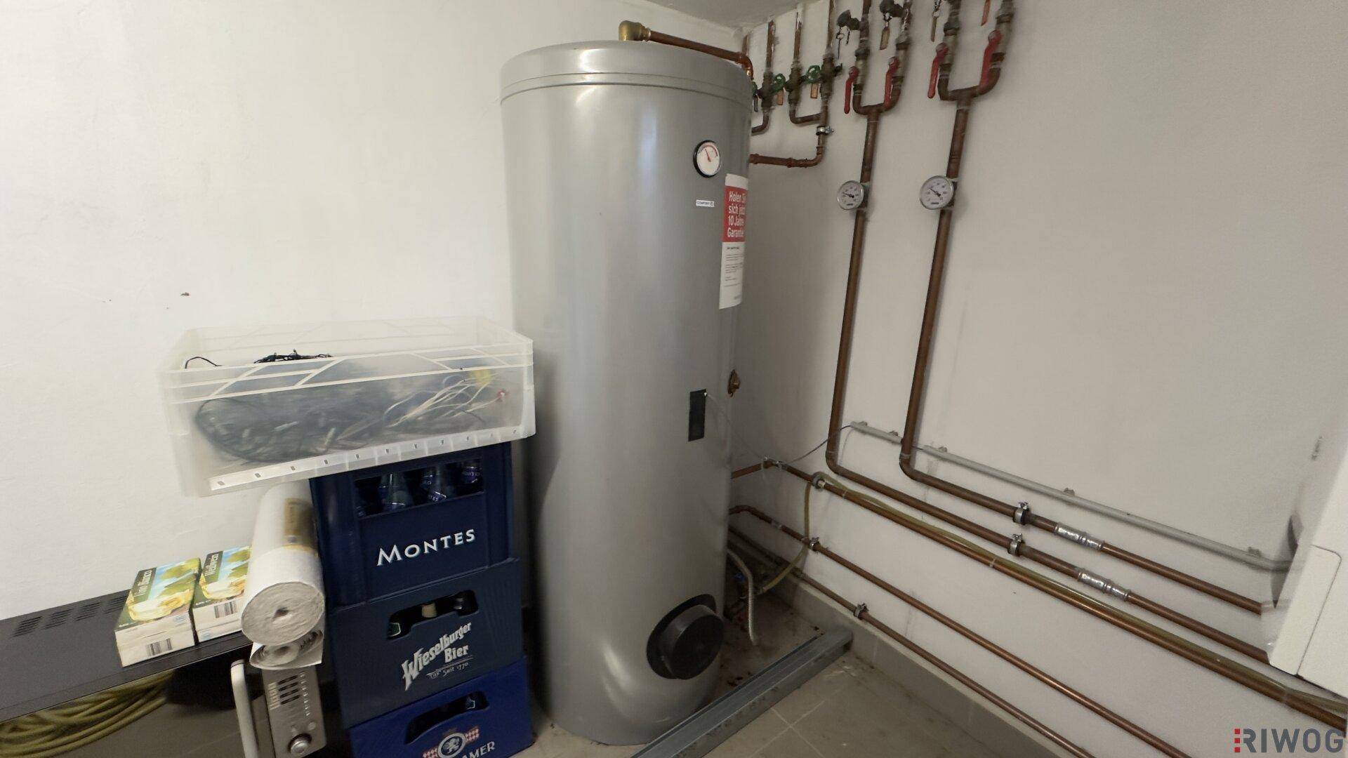 Funktionaler Hauswirtschaftsraum mit einem großen Warmwasserspeicher und sichtbaren Rohrleitungen an der Wand.
