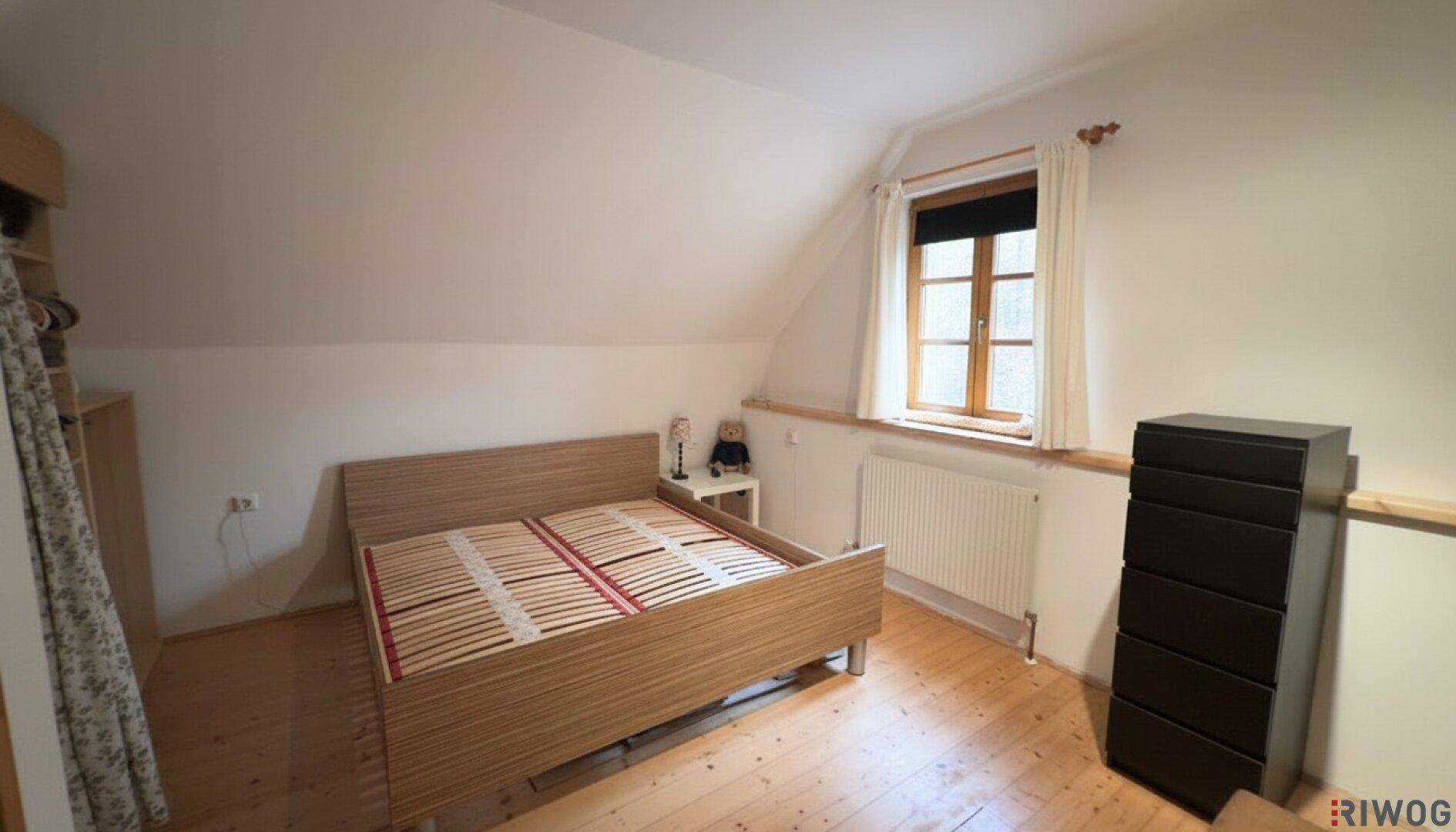 Helles Schlafzimmer mit Holzboden, Dachschräge und einem Fenster, das natürliches Licht hereinlässt.