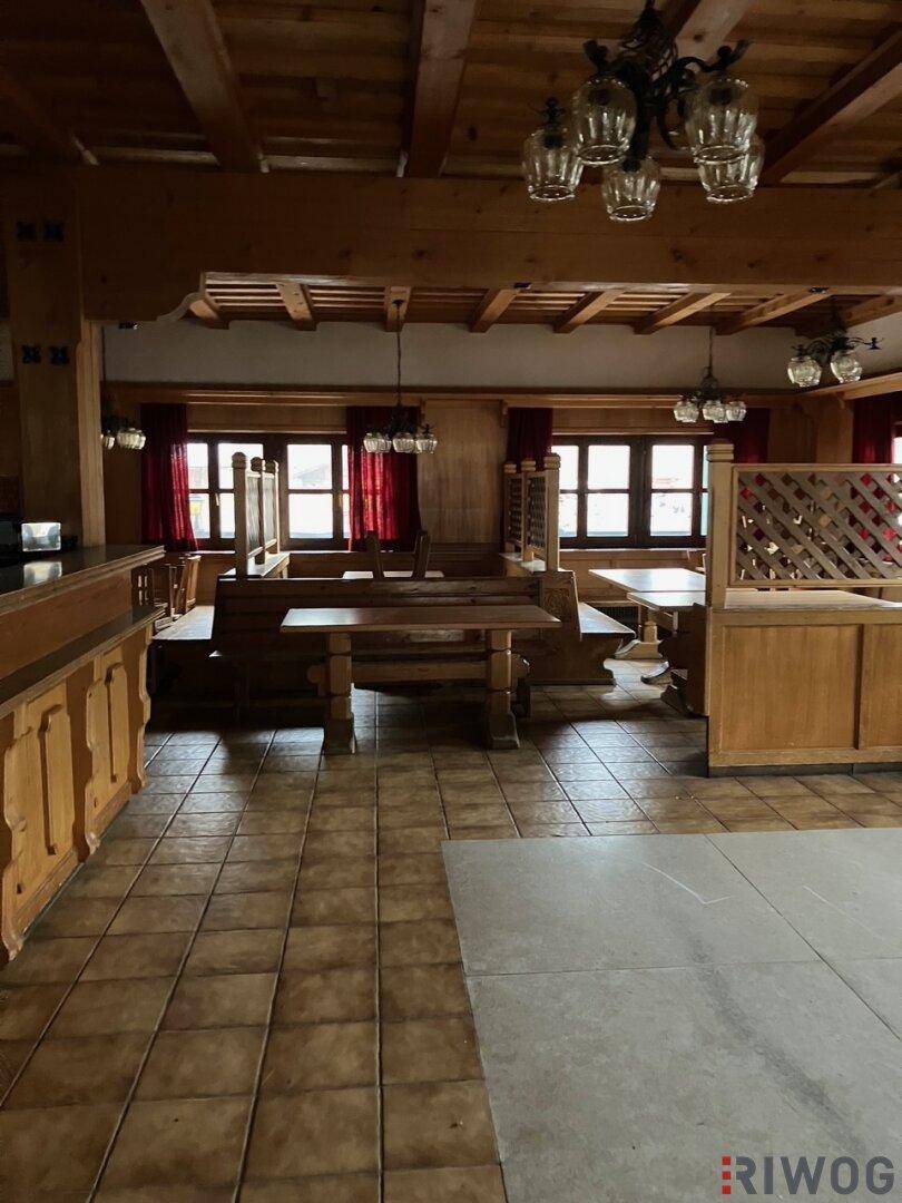 Rustikaler Speisesaal mit Holzbänken, Tischen und einer Bar, typisch für alpine Gasthäuser.