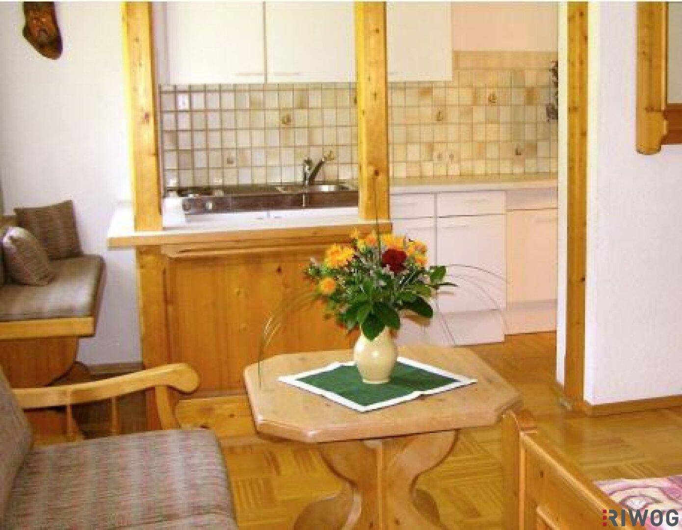 Kleine Küche mit weißen Schränken und Holzdetails, offen zum Wohnbereich.
