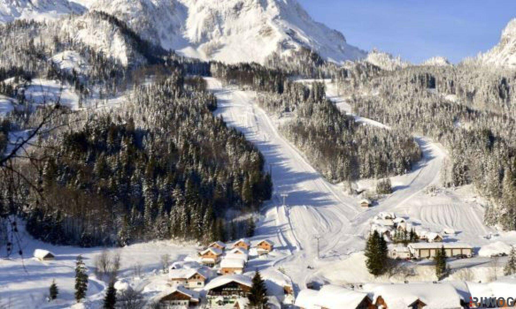 Weitläufige Winterlandschaft mit schneebedeckten Bergen, Wäldern und präparierten Skipisten.