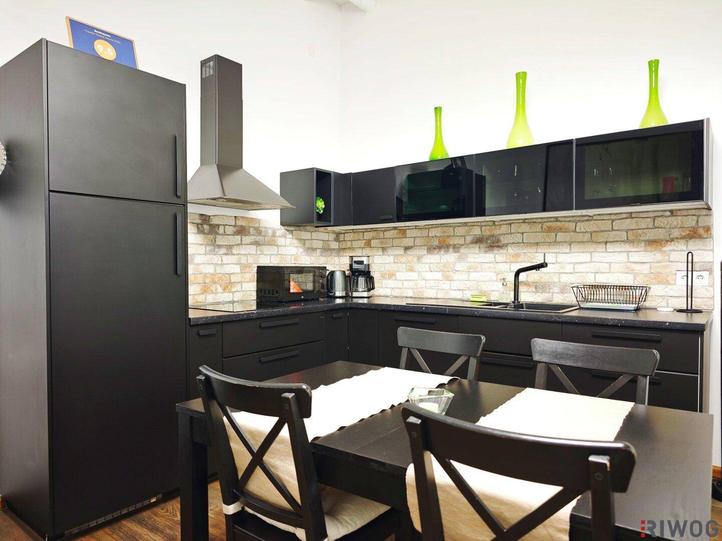 Moderne schwarze Küche mit Backsteinwand und Esstisch im offenen Wohnbereich.