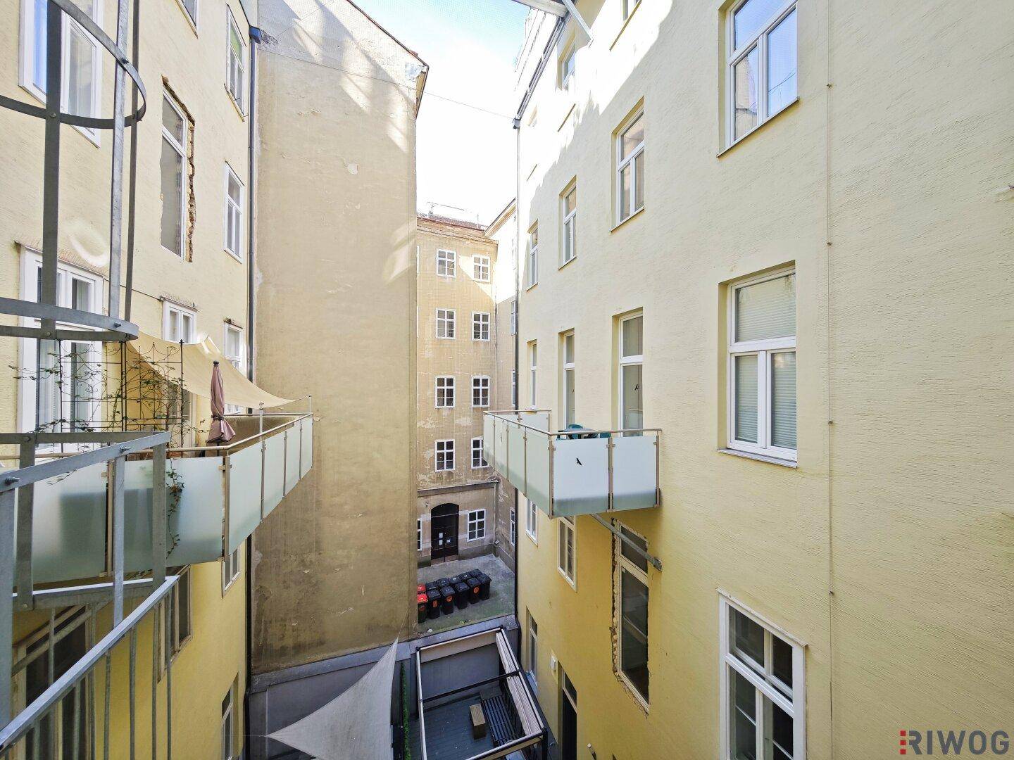 Blick von oben in einen engen Innenhof mit mehreren Balkonen und Gebäudefassaden.