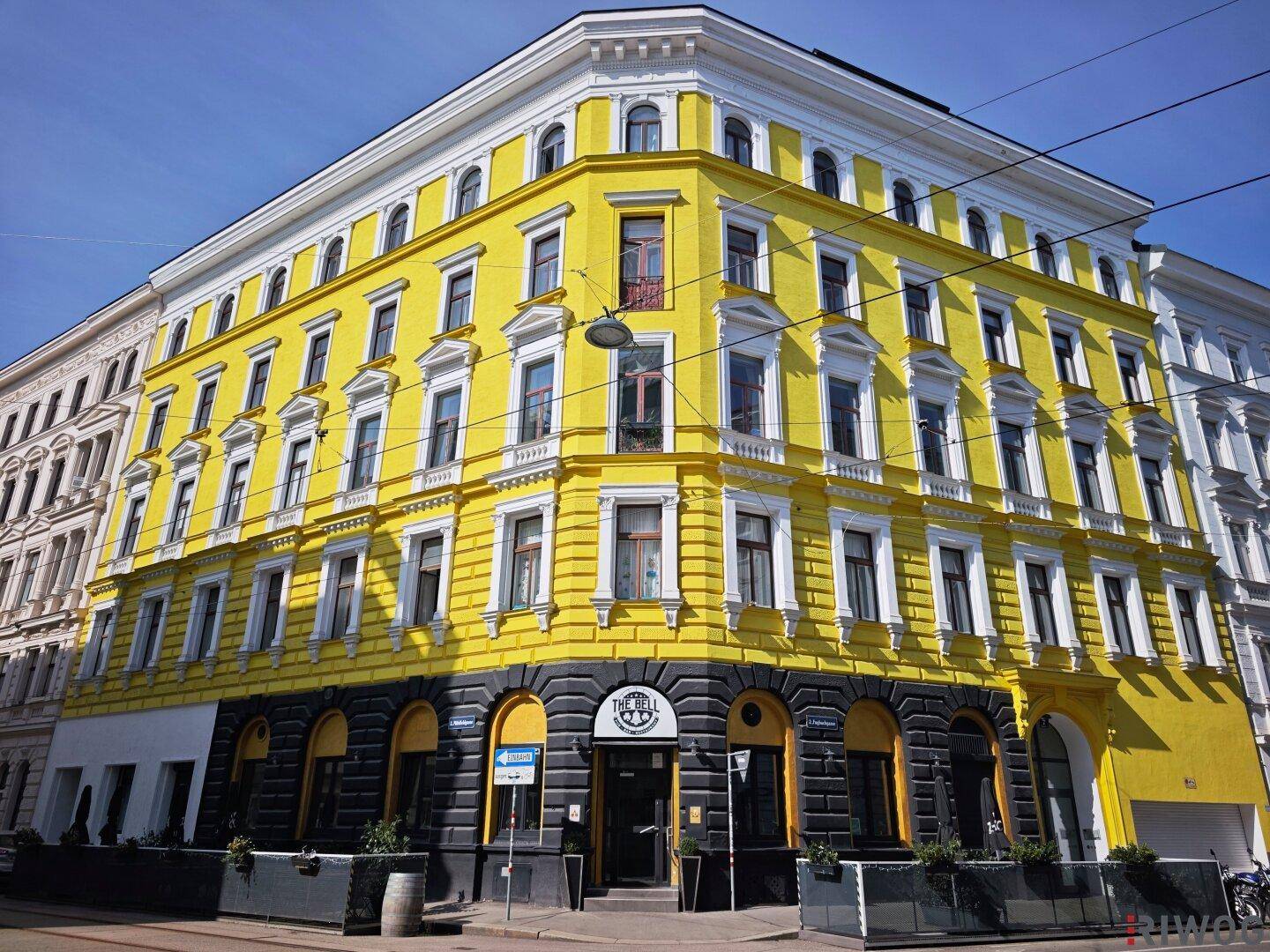 Historisches Eckgebäude mit auffälliger gelber Fassade und vielen Fenstern.