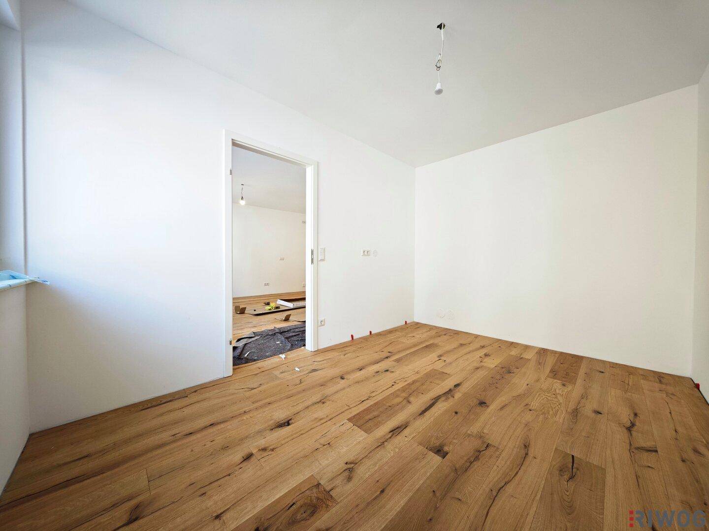Geräumiger, heller Raum mit neuem Holzboden und Blick in angrenzendes Zimmer.