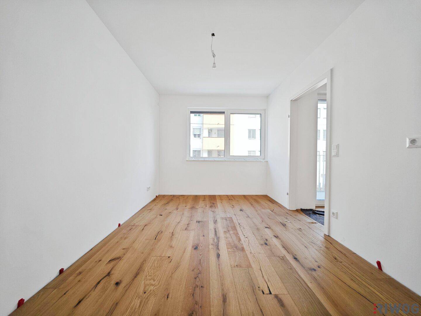 Leerer Raum mit frisch verlegtem Holzboden und großen Fenstern, bereit zum Einzug.