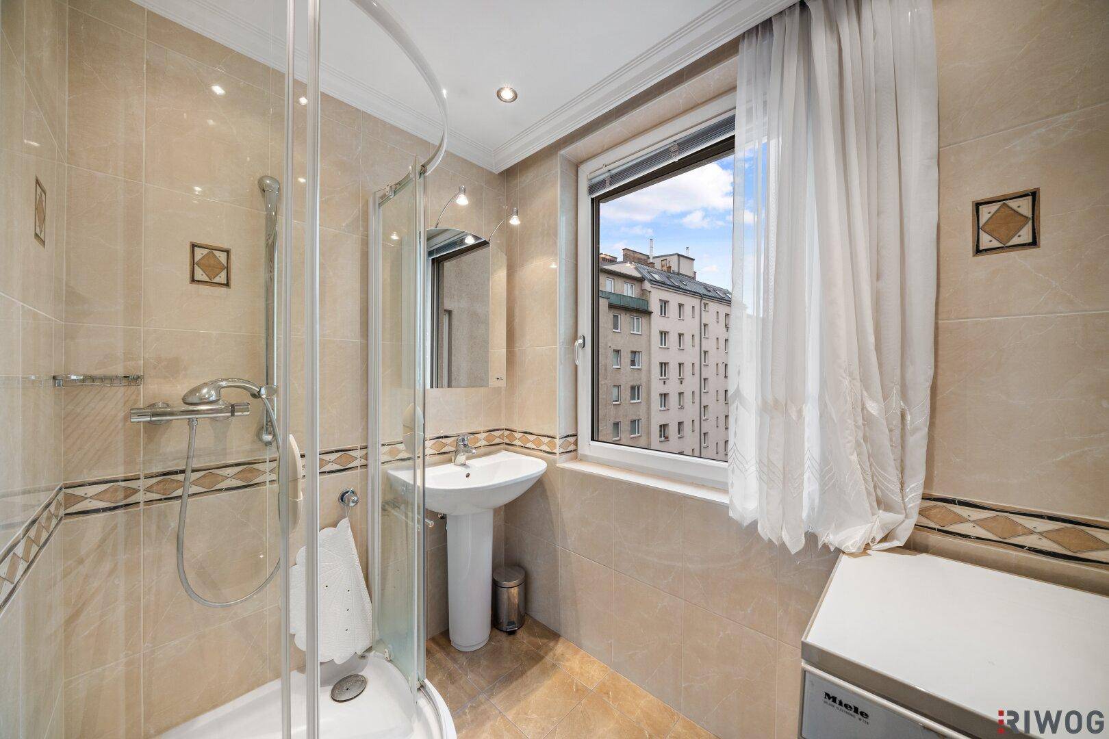 Badezimmer mit Duschkabine, Waschbecken und Fenster für Tageslicht.