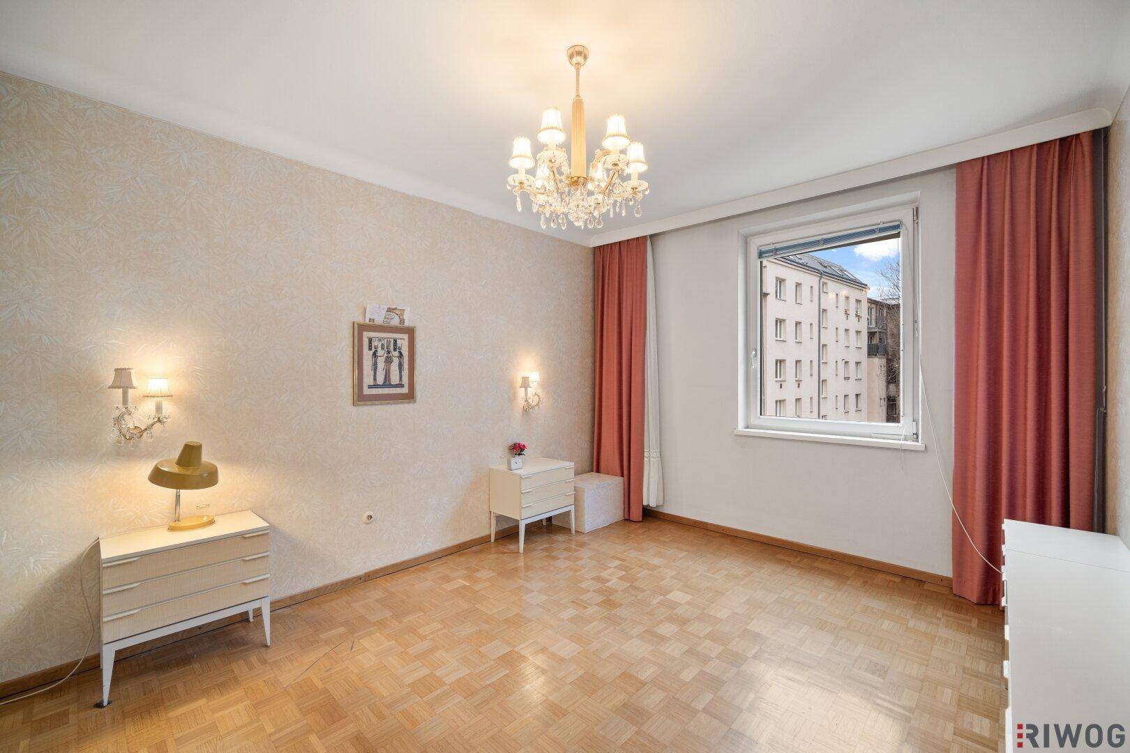 Helles Schlafzimmer mit Parkettboden, Fenster und Blick auf die umliegenden Gebäude.