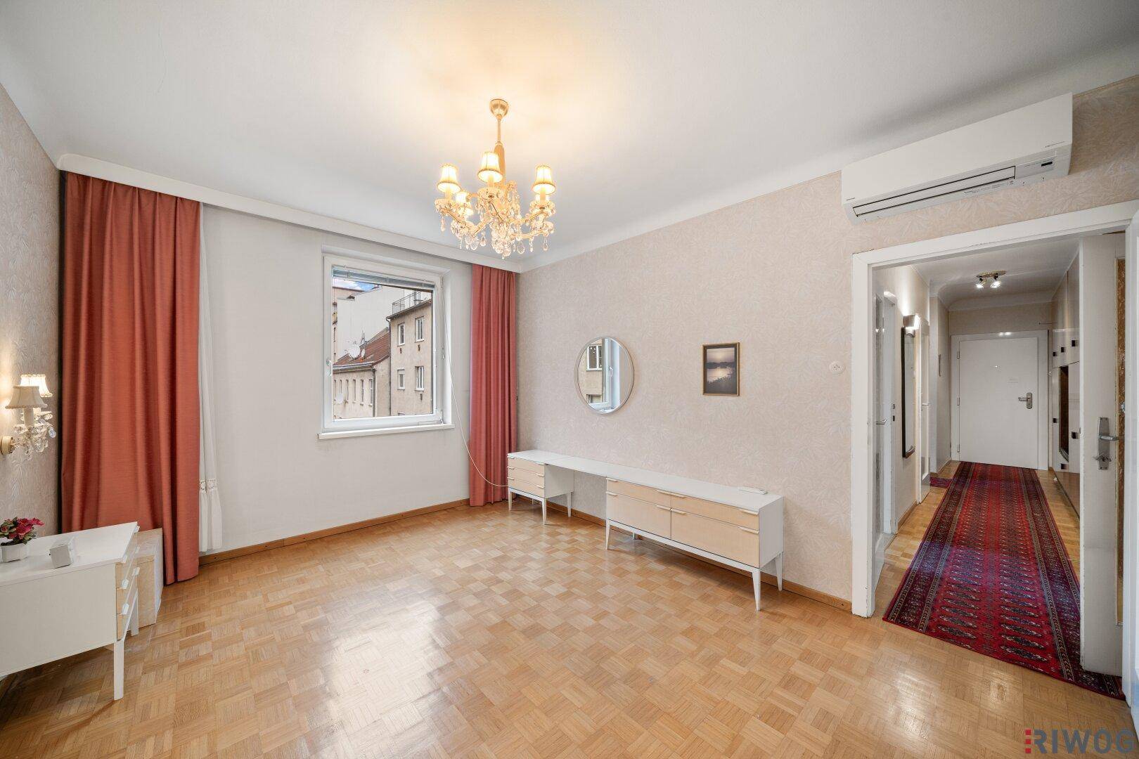 Schlafzimmer mit Parkettboden, Fenster und Zugang zum Flur.