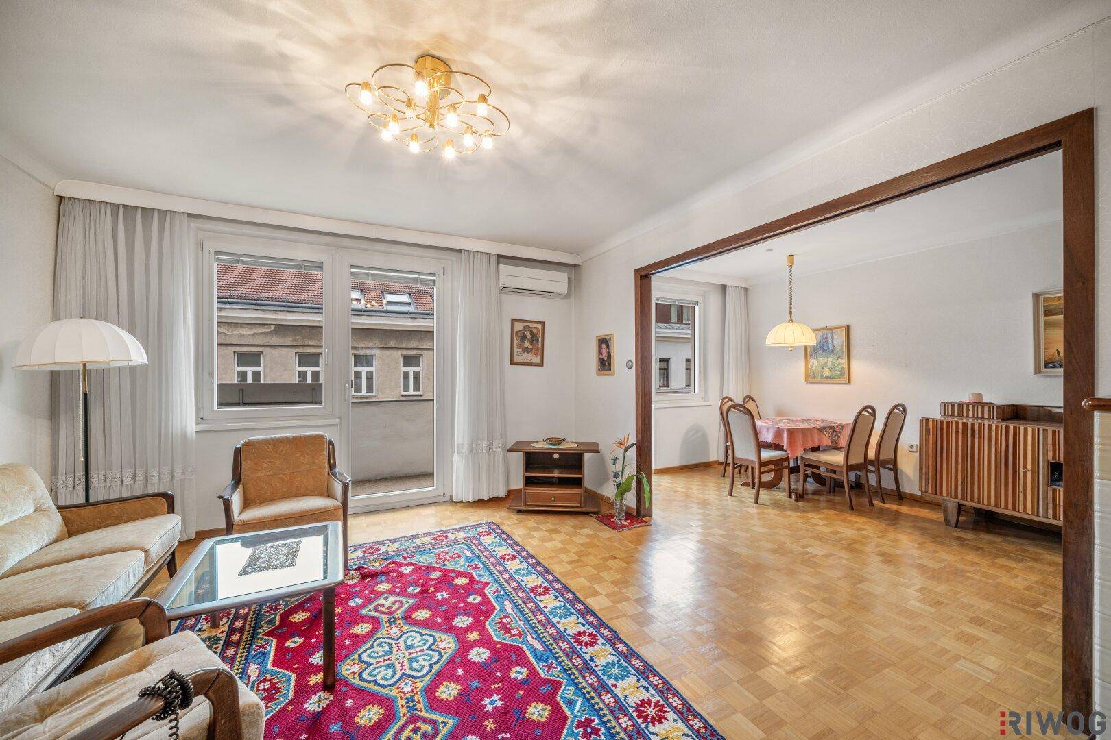 Geräumiger Wohn-Essbereich mit Parkettboden, vintage Möbeln und Zugang zum Balkon.