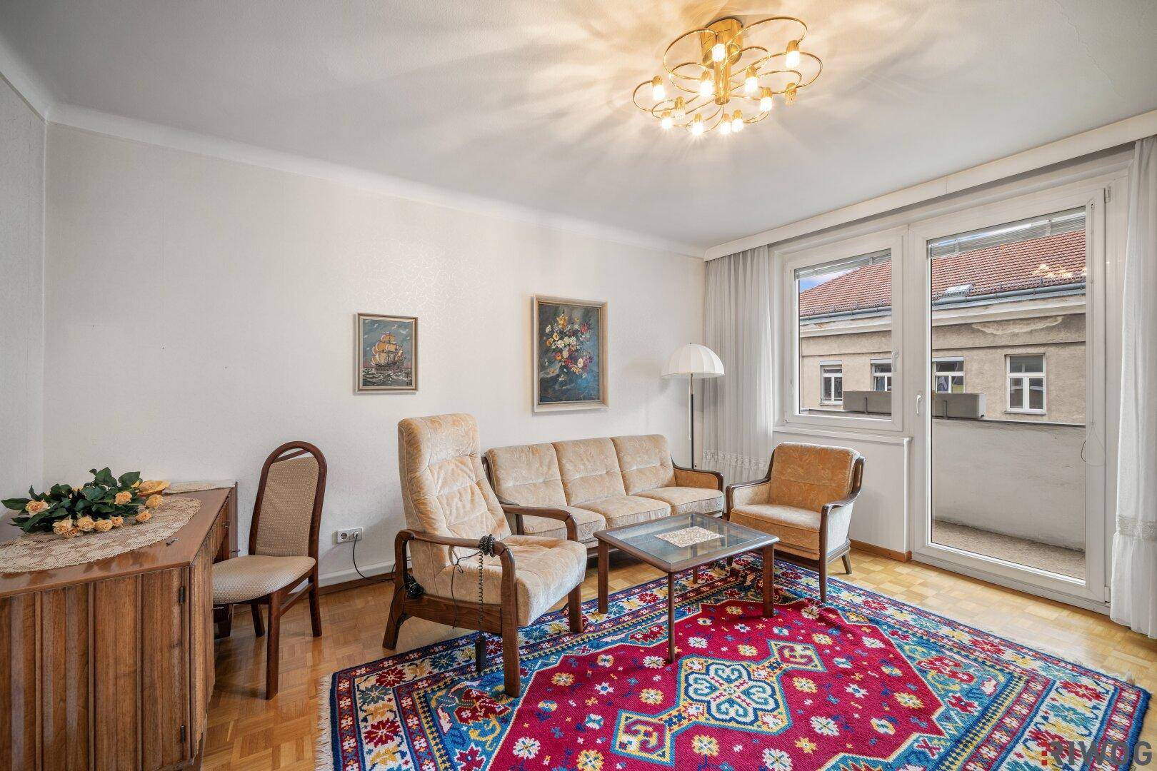 Gemütliches Wohnzimmer mit Parkettboden, beigen Sofas und einem farbenfrohen Teppich.