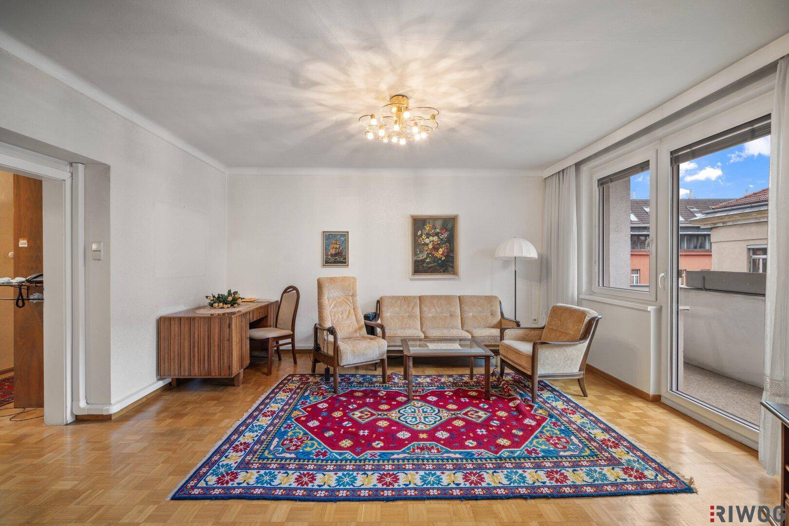 Wohnzimmer mit Parkettboden, Schreibtisch und Zugang zum Außenbereich.