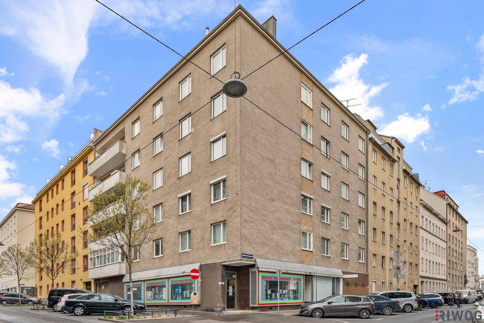 Mehrstöckiges Wohngebäude an einer Straßenecke mit Geschäften im Erdgeschoss.