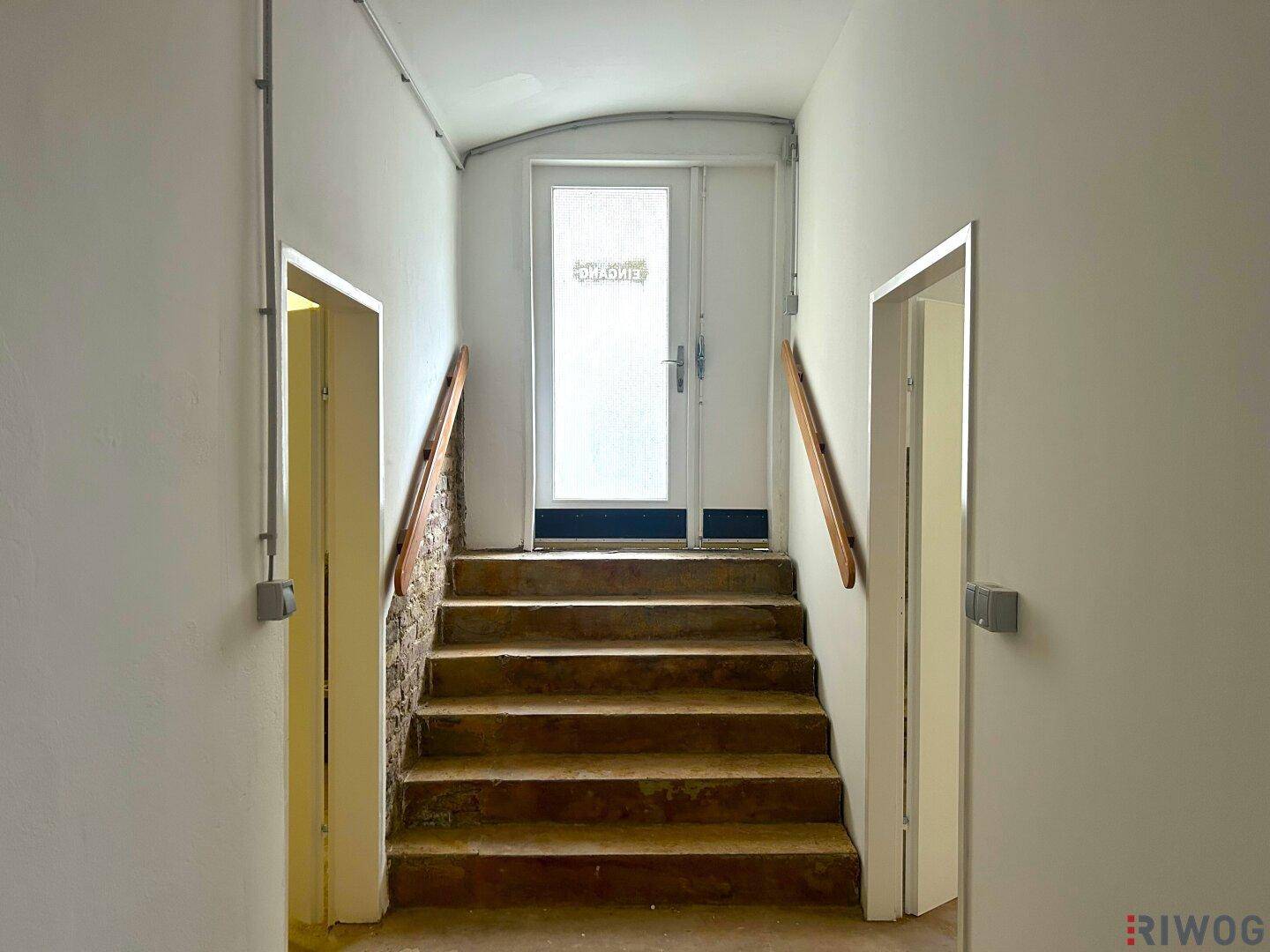 Treppenhaus mit Holzgeländer und einer Tür am oberen Ende, die zu einem weiteren Bereich führt.