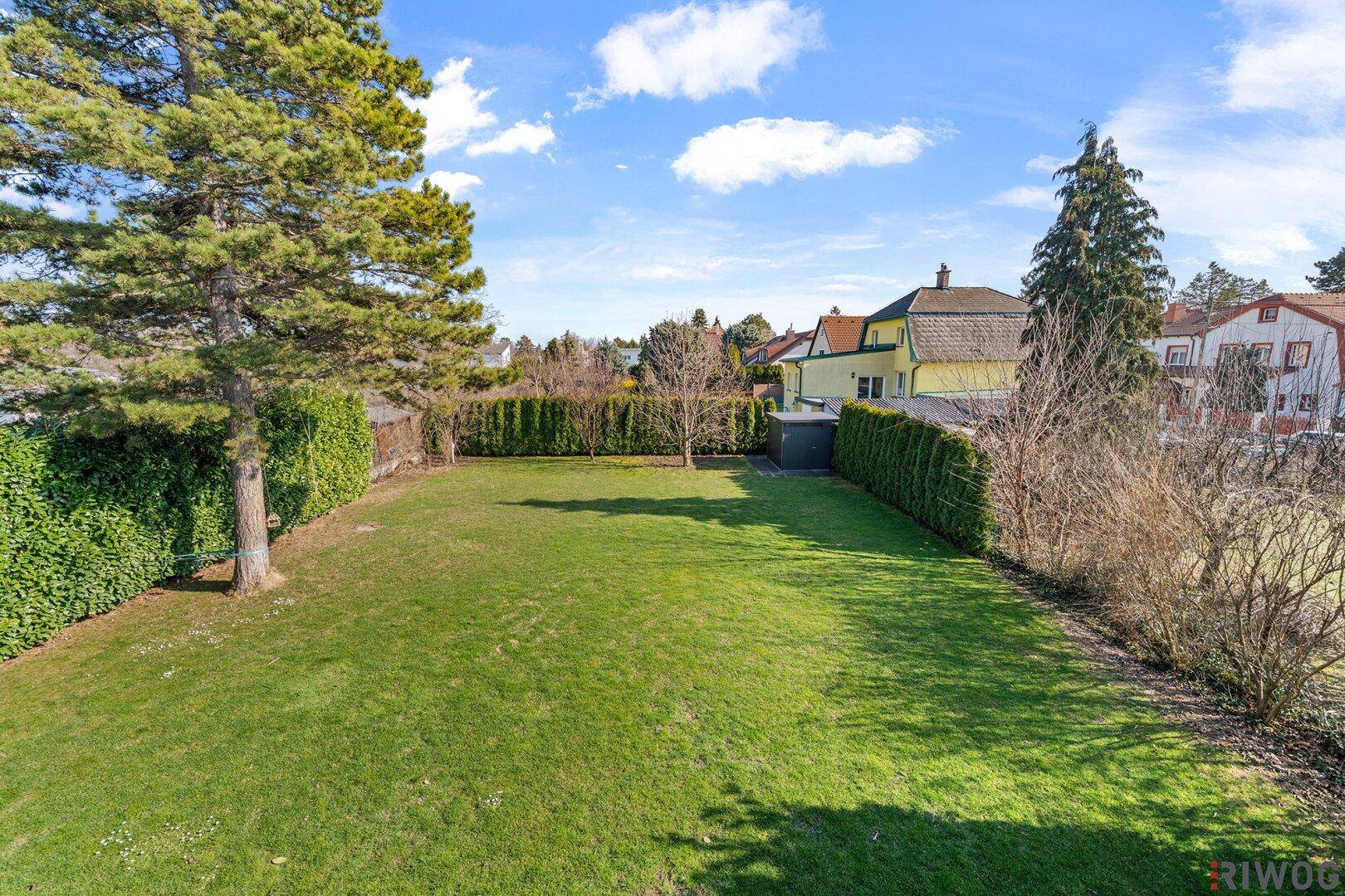 Weitläufiger, gepflegter Garten mit Rasenfläche und hohen Hecken für Privatsphäre.