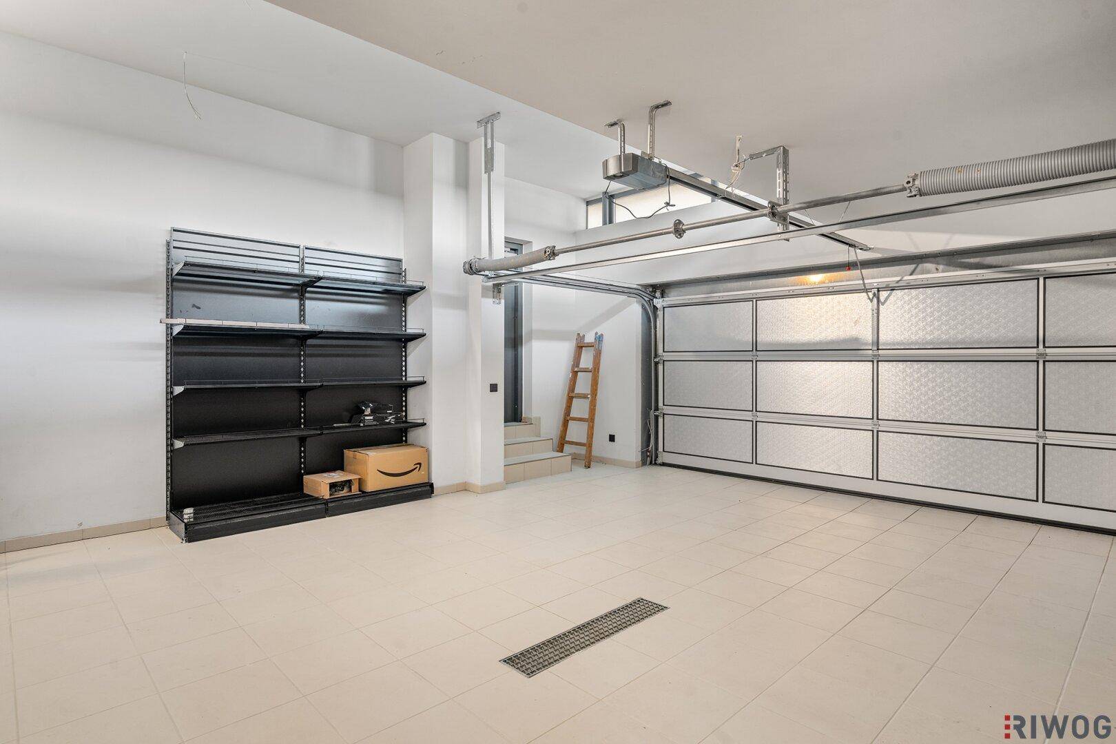 Geräumige Garage mit Fliesenboden, Regalsystem und automatischem Garagentor.