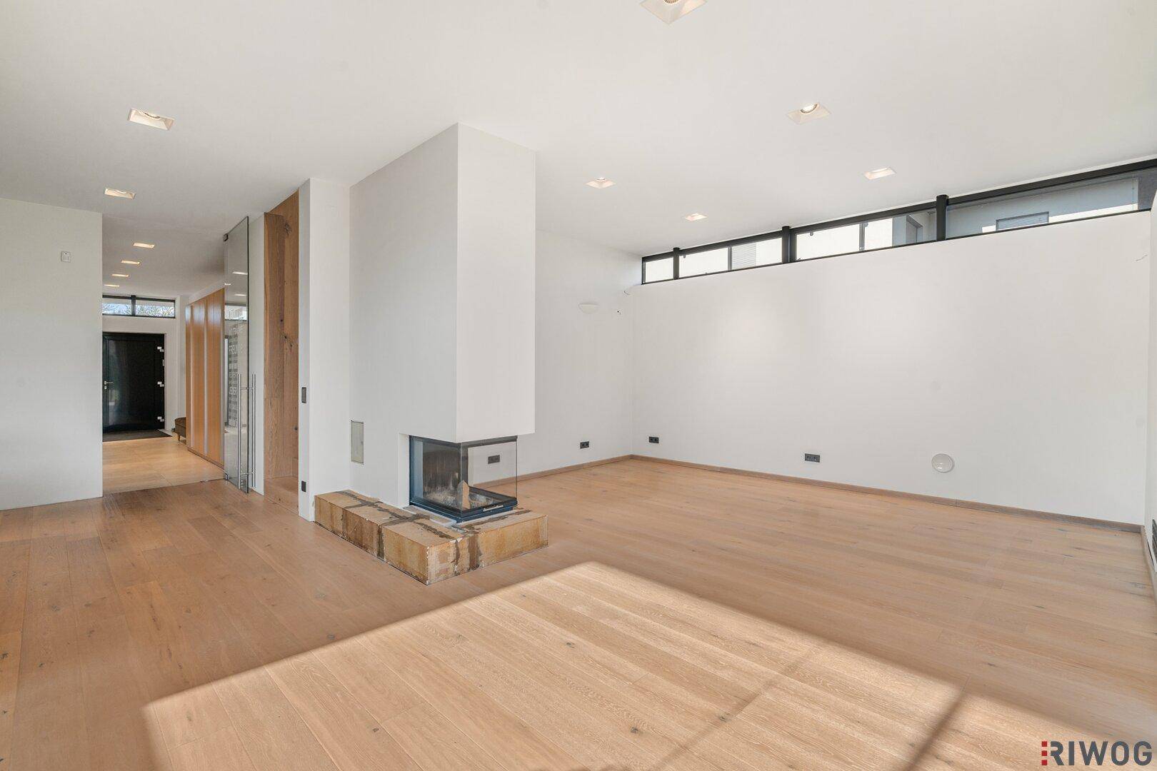 Geräumiges Wohnzimmer mit Kamin, Holzboden und viel Tageslicht durch hohe Fenster.