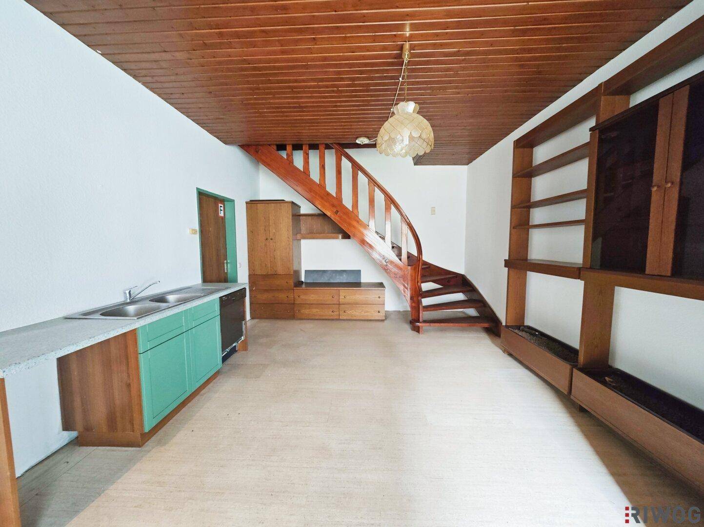 Wohnbereich mit Holzdecke, integrierter Küchenzeile und einer geschwungenen Holztreppe.