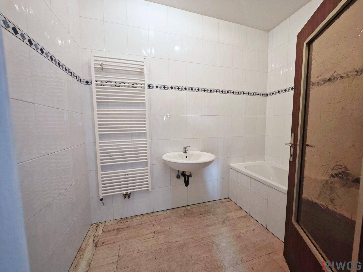Badezimmer mit weißen Fliesen, Badewanne und Handtuchheizkörper, bereit zur Renovierung.