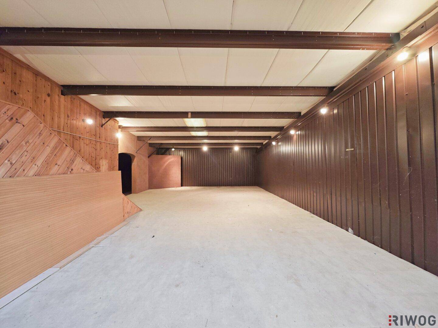 Langer Lagerraum mit Holzverkleidung an einer Wand und sichtbaren Deckenbalken.