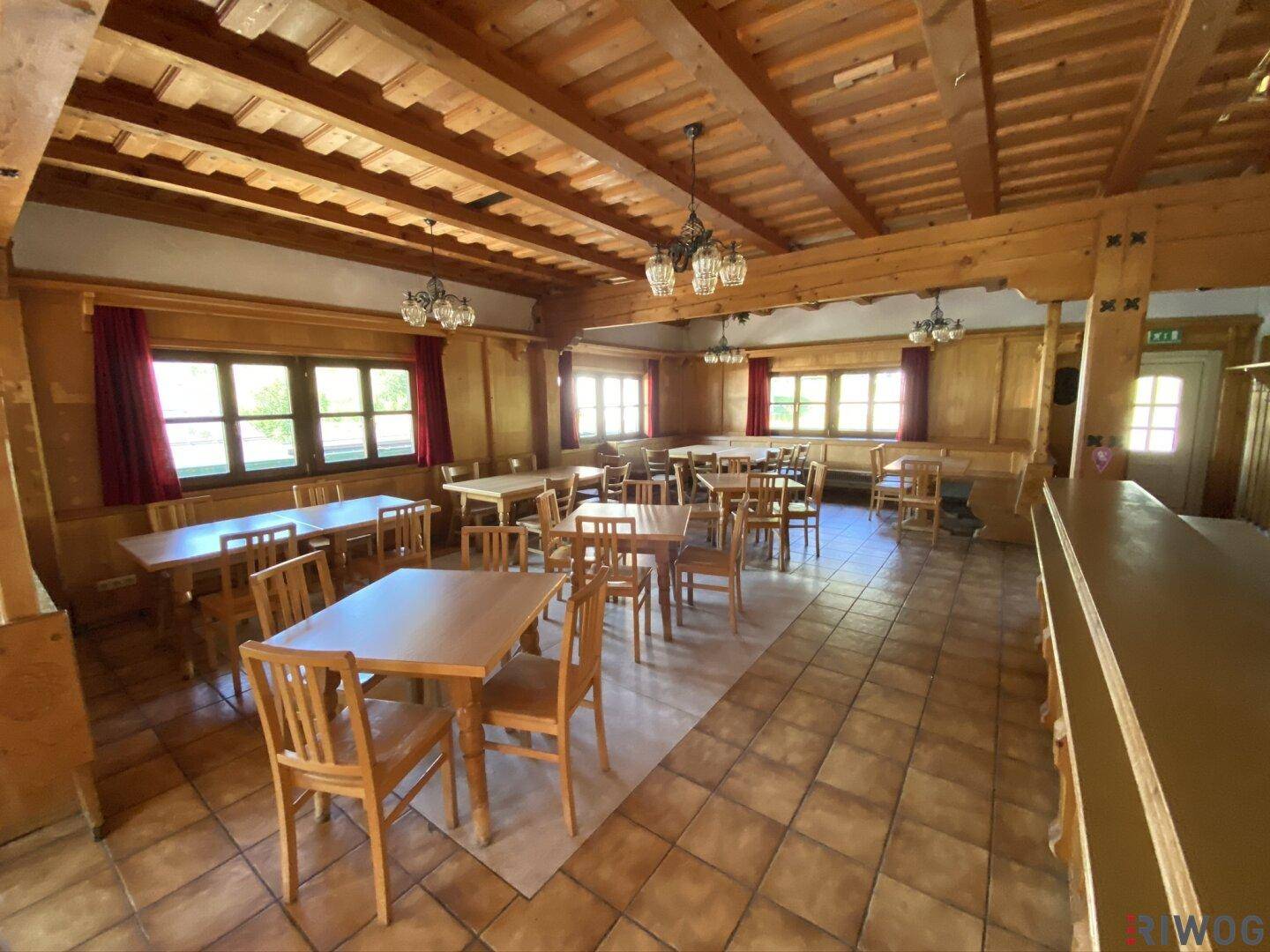Geräumiger Speisesaal mit Holztischen, Stühlen und rustikalen Holzbalken an der Decke.
