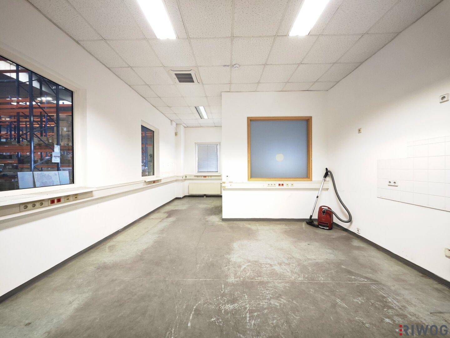 Helles, leeres Büro mit weißen Wänden, Fenstern und einem praktischen Betonboden für vielseitige Nutzung.