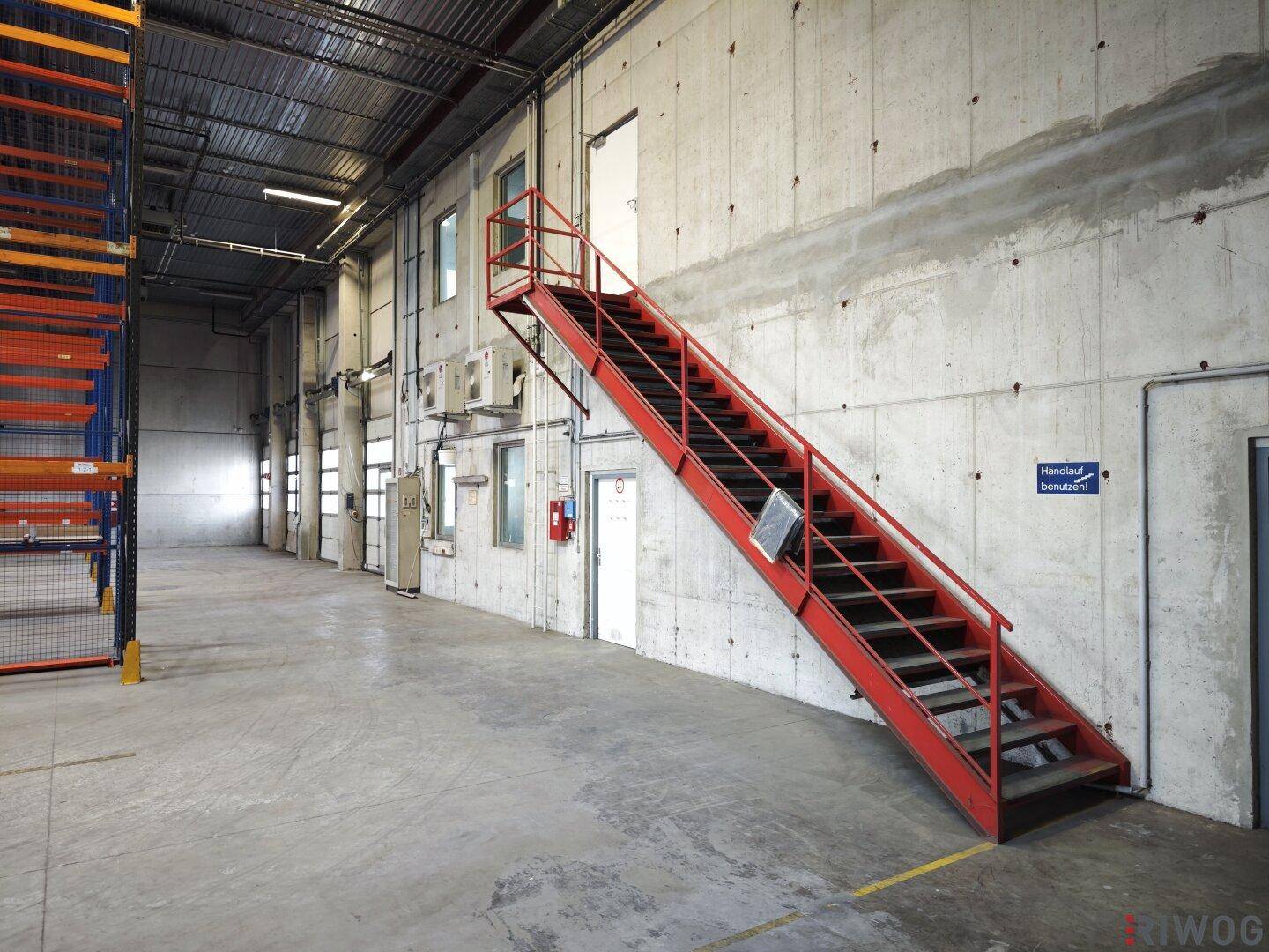 Industrielle Lagerhalle mit roter Metalltreppe, Betonwänden und Klimaanlagen an der Wand.