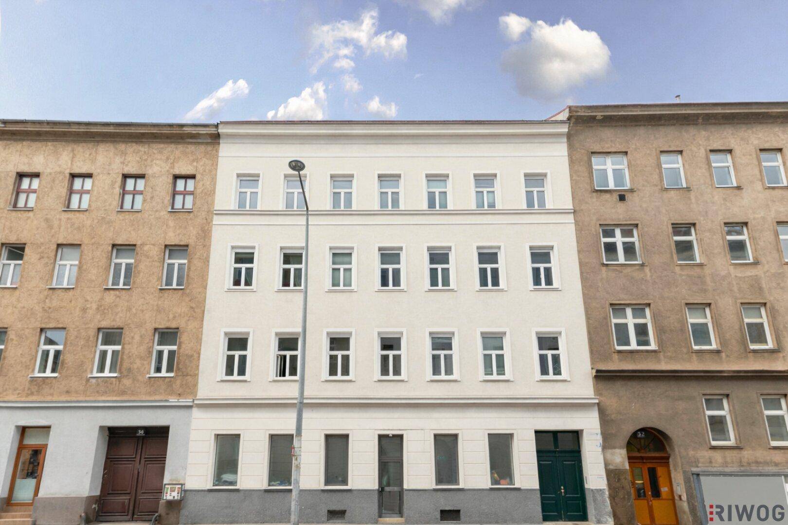Renovierte Fassade eines Altbaus in der Stadt mit vielen Fenstern und klarem Himmel.