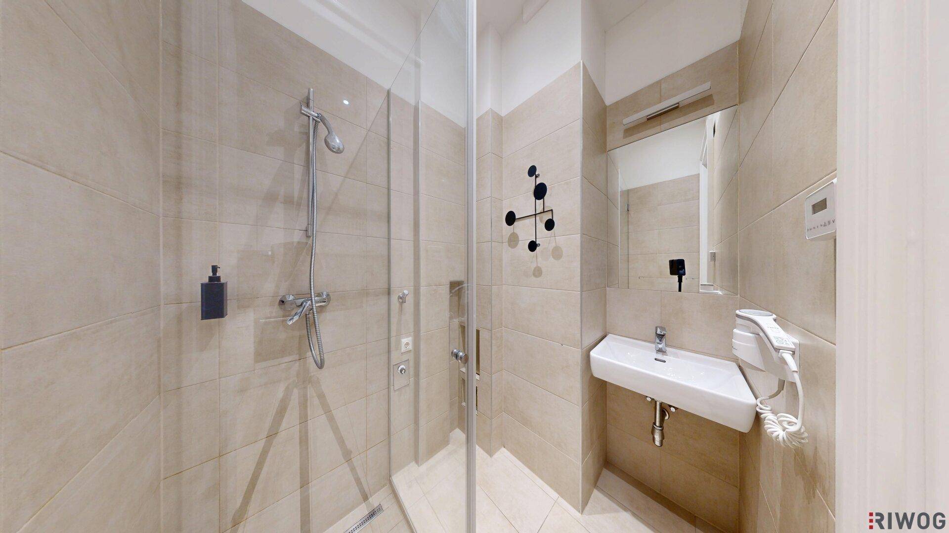 Modernes Badezimmer mit beigefarbenen Fliesen, ebenerdiger Dusche und minimalistischem Waschbecken.