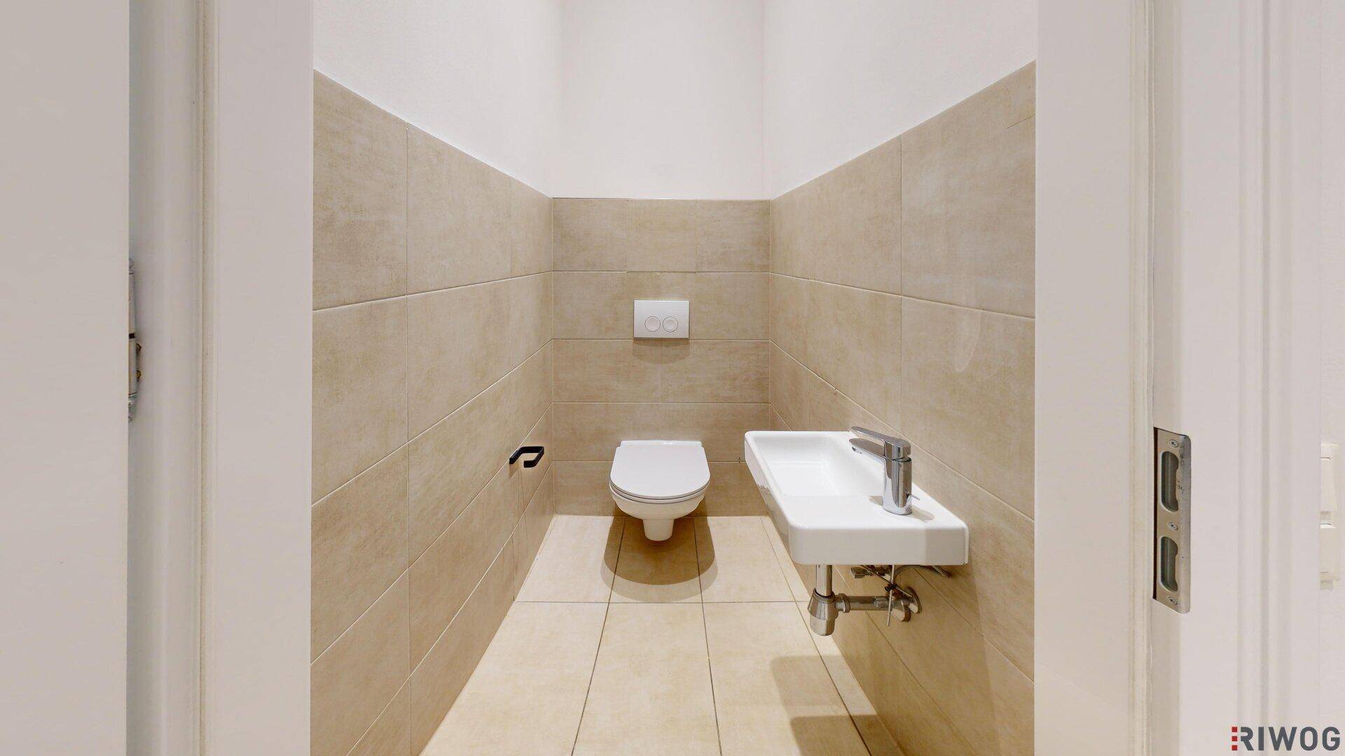 Kleines Gäste-WC mit beigefarbenen Wandfliesen, wandhängendem WC und modernem Waschbecken.