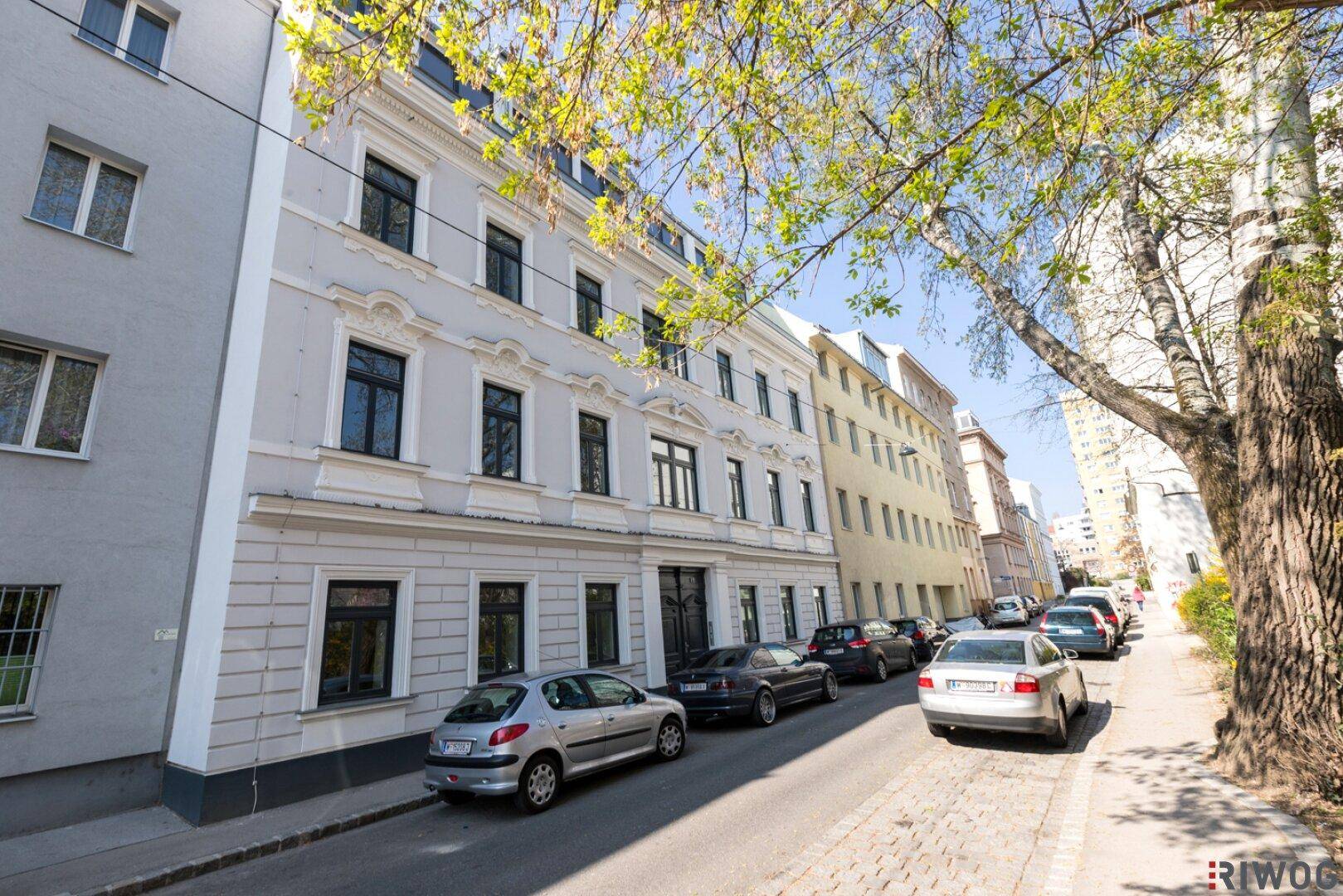 Historisches Wohngebäude an einer belebten Straße mit parkenden Autos und Bäumen.