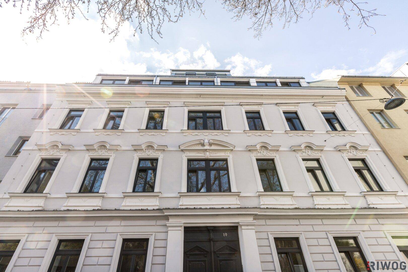 Klassische Fassade eines sanierten Altbaus mit vielen Fenstern und dekorativen Elementen.