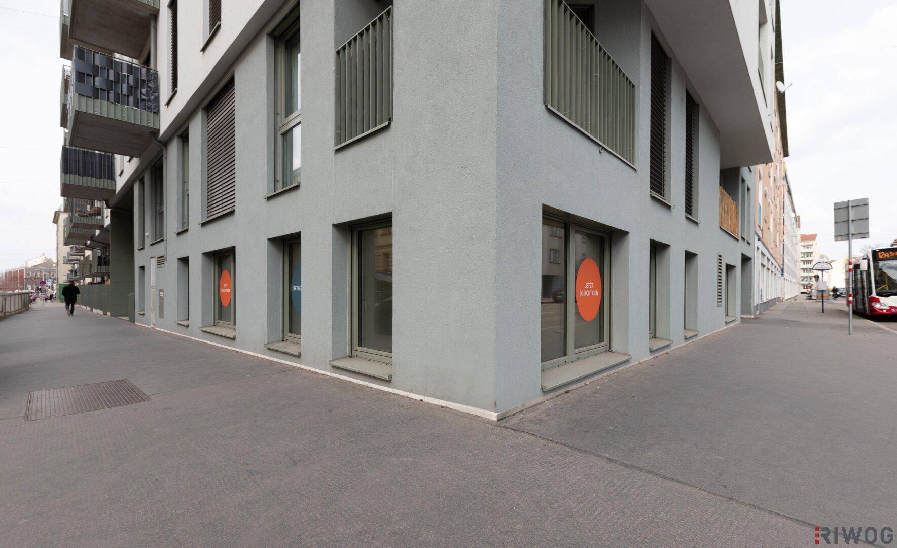 Moderne Gebäudeecke mit großen Schaufenstern im Erdgeschoss an einer belebten Straße.