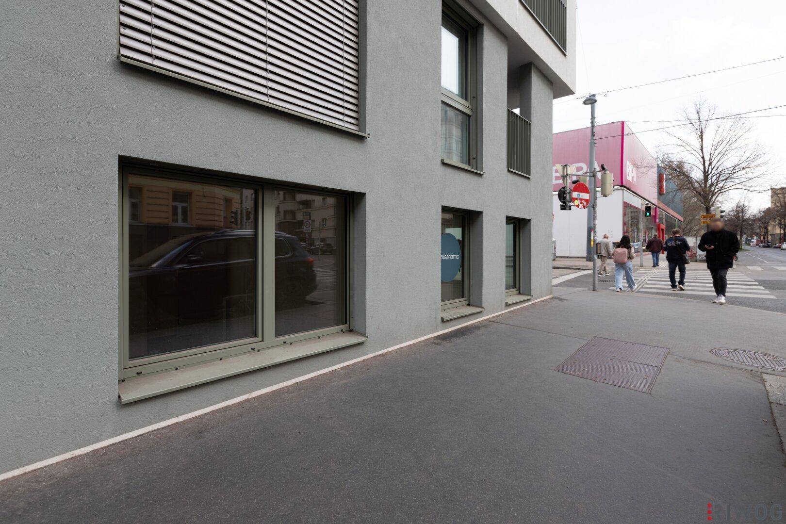 Fassade eines modernen Gebäudes mit großen Fenstern und Blick auf die belebte Straße.