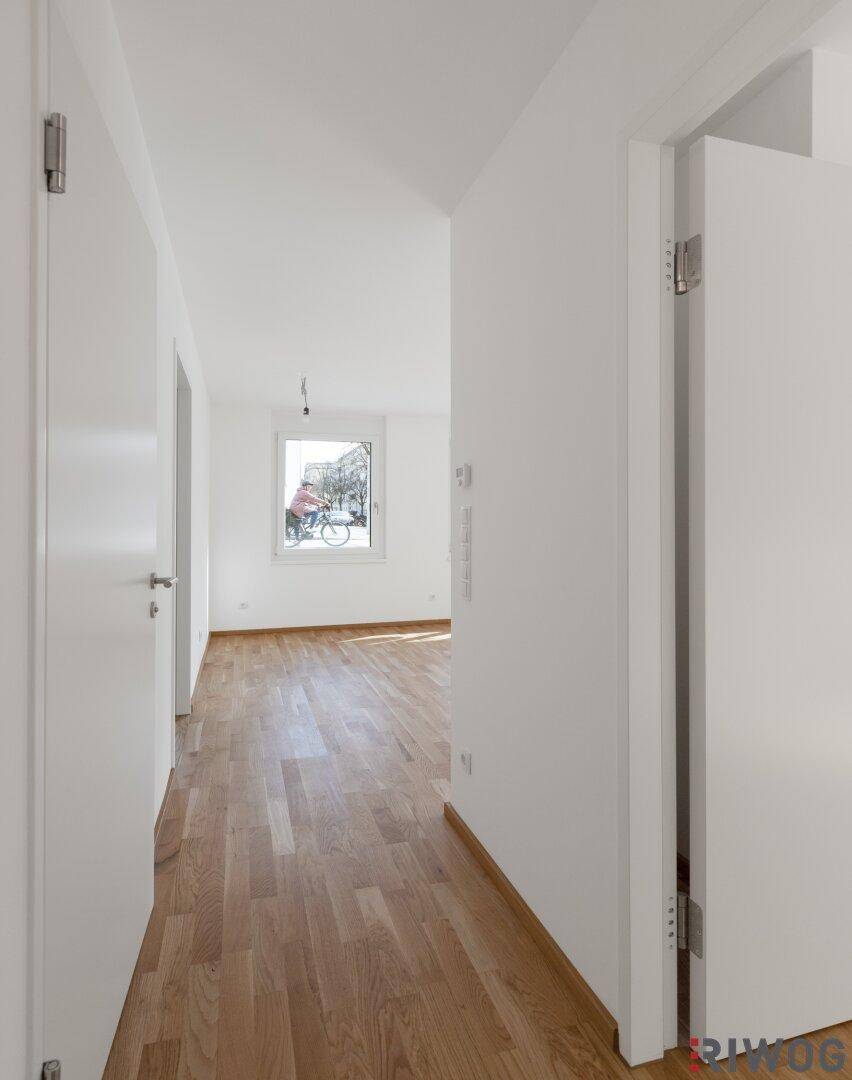 Heller Flur mit Holzboden und weißen Wänden, der zu weiteren Räumen führt.