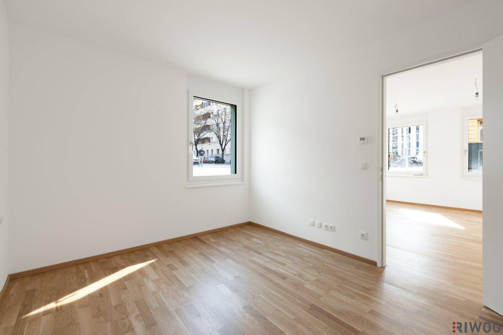 Leerer Raum mit Holzboden und einem Fenster, das Tageslicht hereinlässt, ideal als Büro.