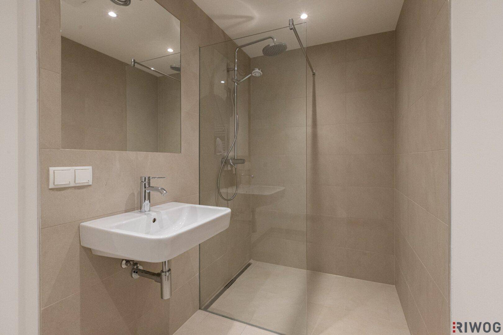 Modernes Badezimmer mit ebenerdiger Dusche, wandhängendem Waschbecken und beigefarbenen Fliesen.