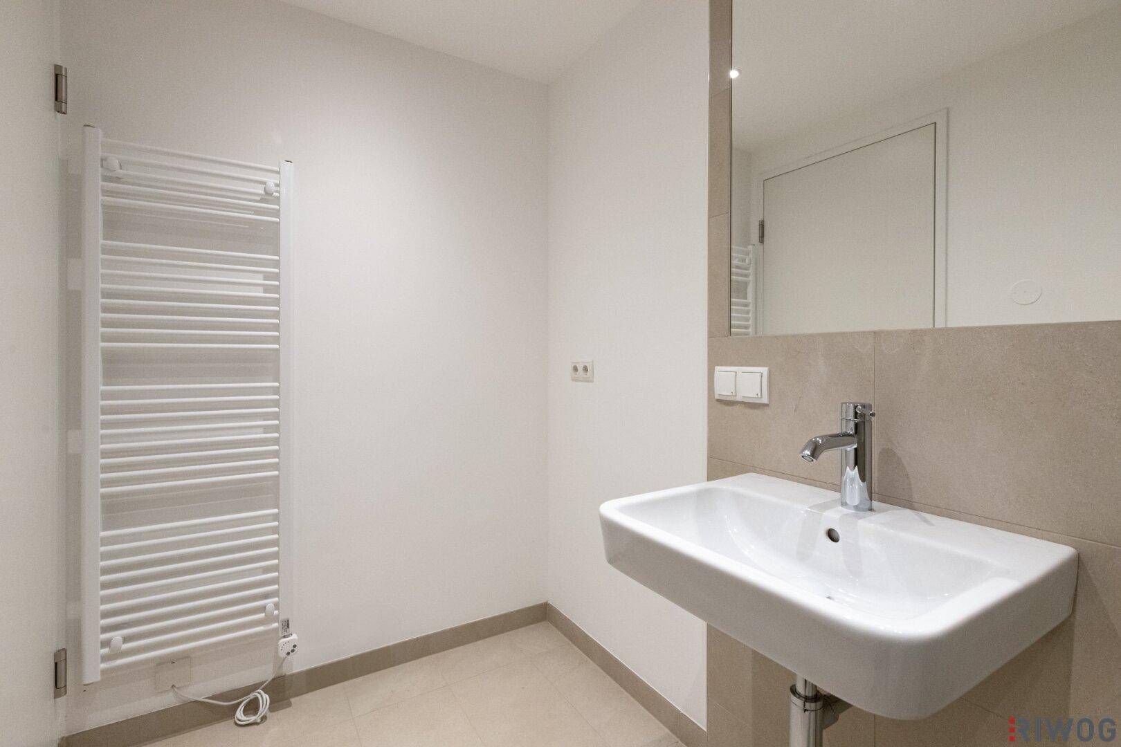 Modernes Badezimmer mit wandhängendem Waschbecken, Spiegel und einem praktischen Handtuchheizkörper.