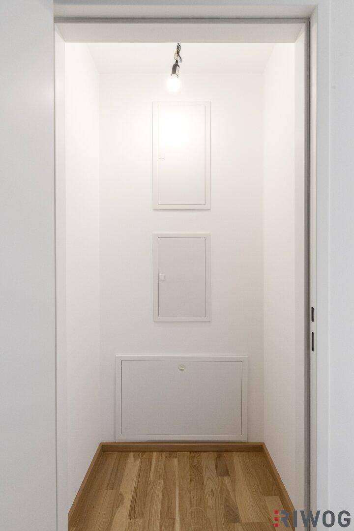 Kleiner Abstellraum oder Nische mit Zugangsklappen an der Wand und Holzboden.