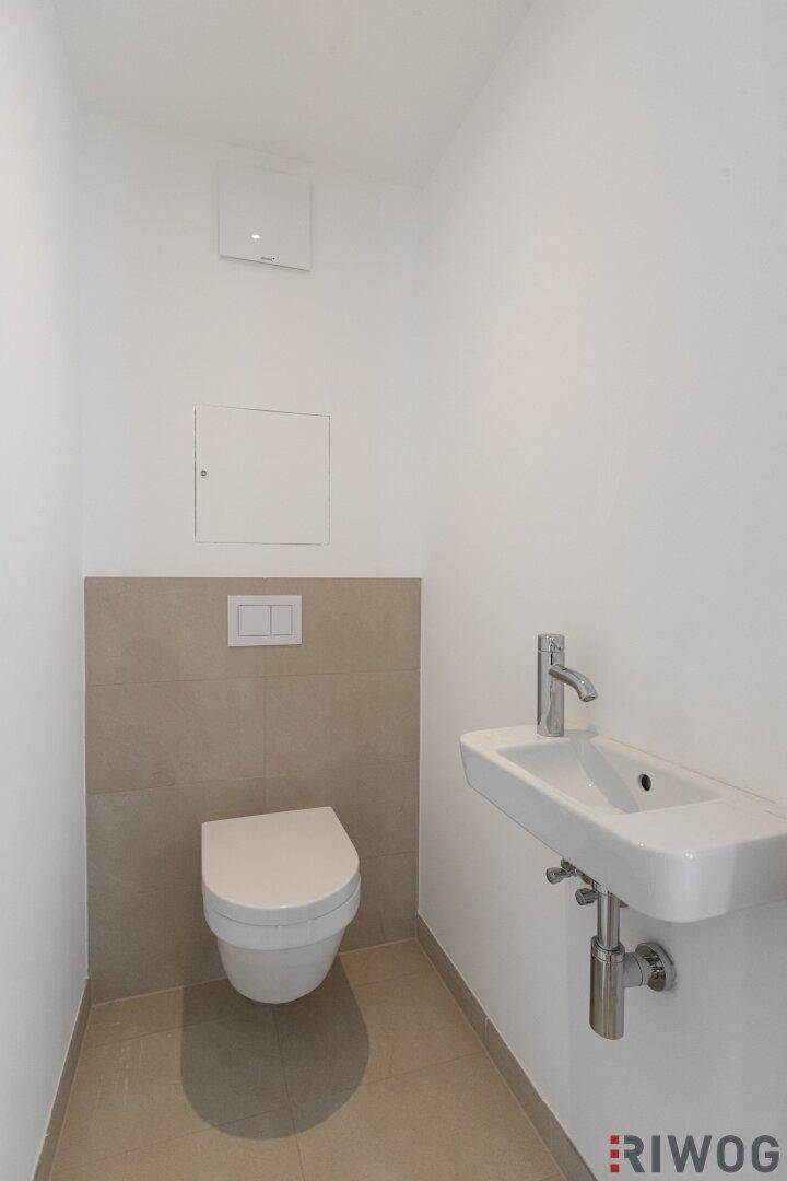 Modernes Gäste-WC mit wandhängender Toilette, Waschbecken und beigefarbenen Wandfliesen.