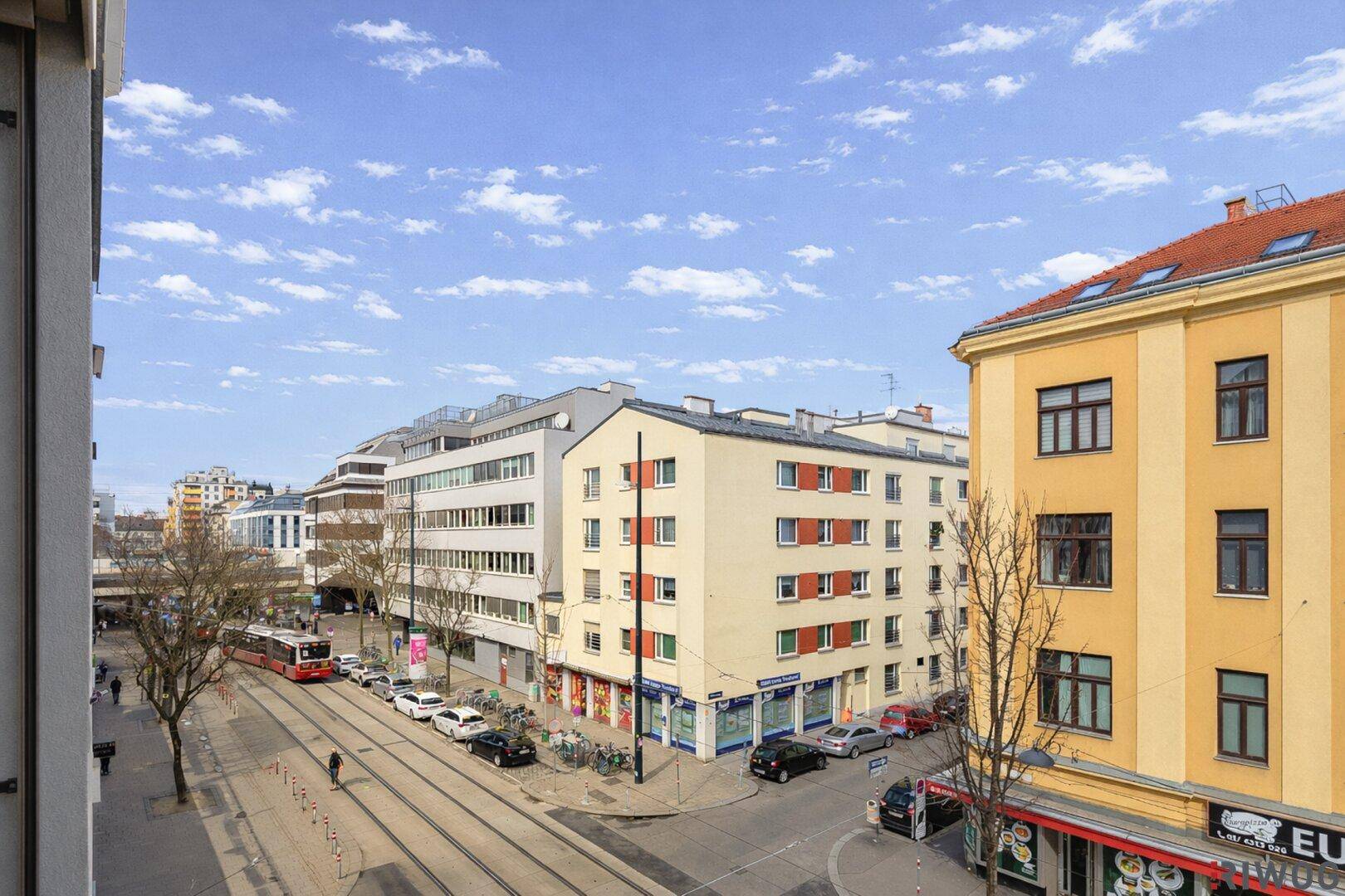 Blick von oben auf eine belebte Stadtstraße mit Gebäuden und einer Straßenbahn.