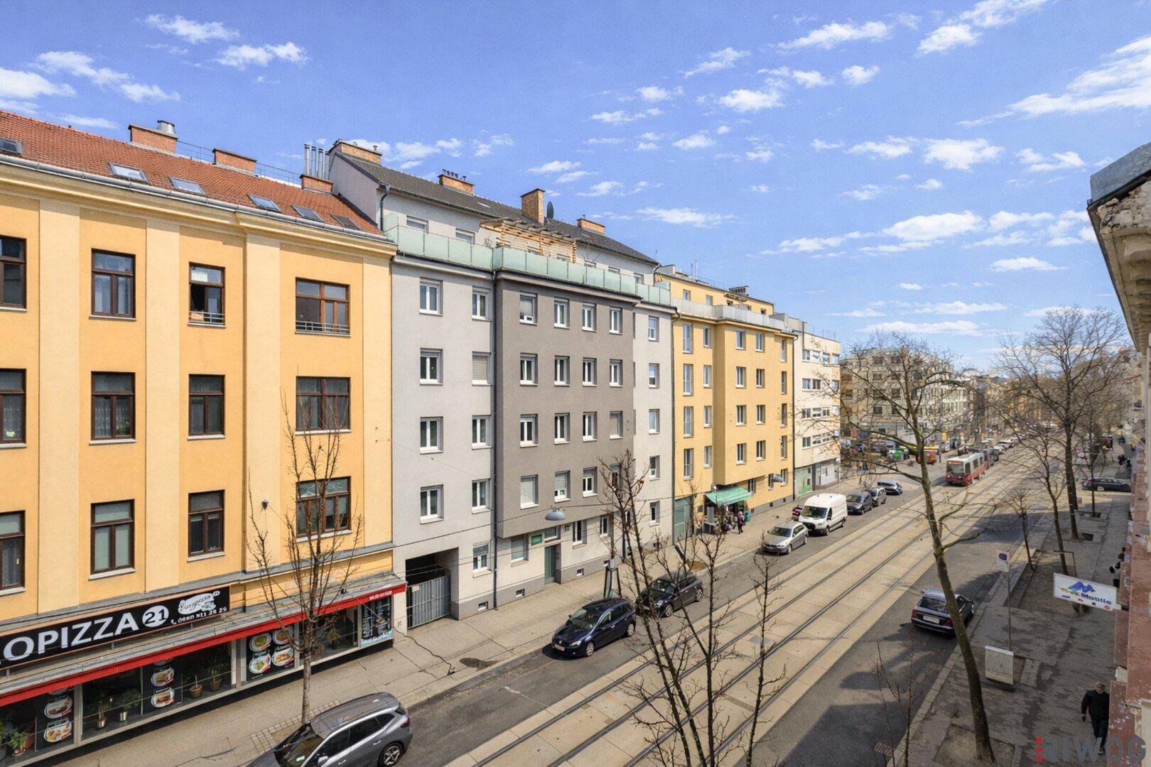 Weitläufiger Blick auf eine städtische Straße mit Gebäuden und vorbeifahrenden Fahrzeugen.