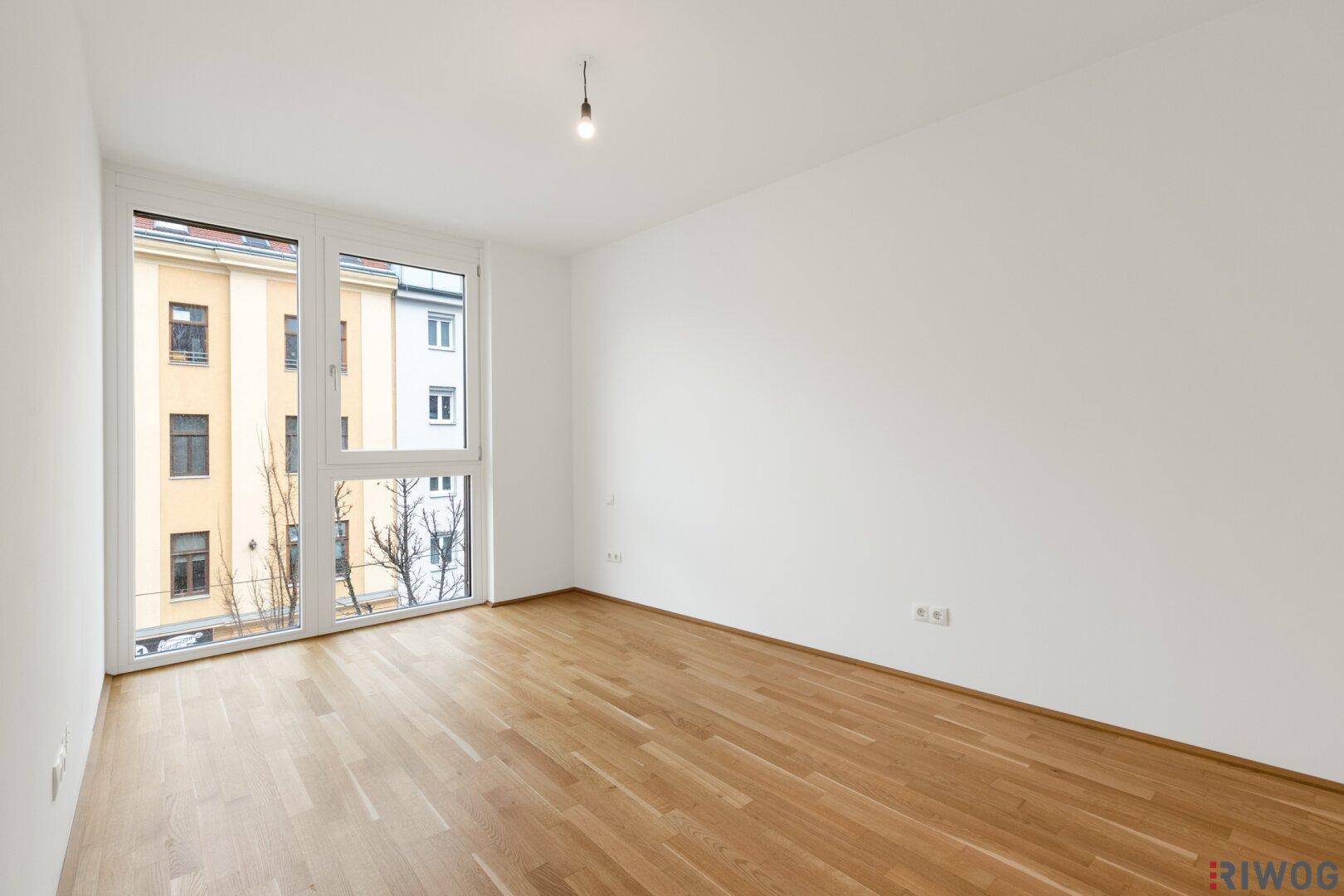 Helles, leeres Schlafzimmer mit großen Fenstern und Holzboden, ideal für persönliche Einrichtung.