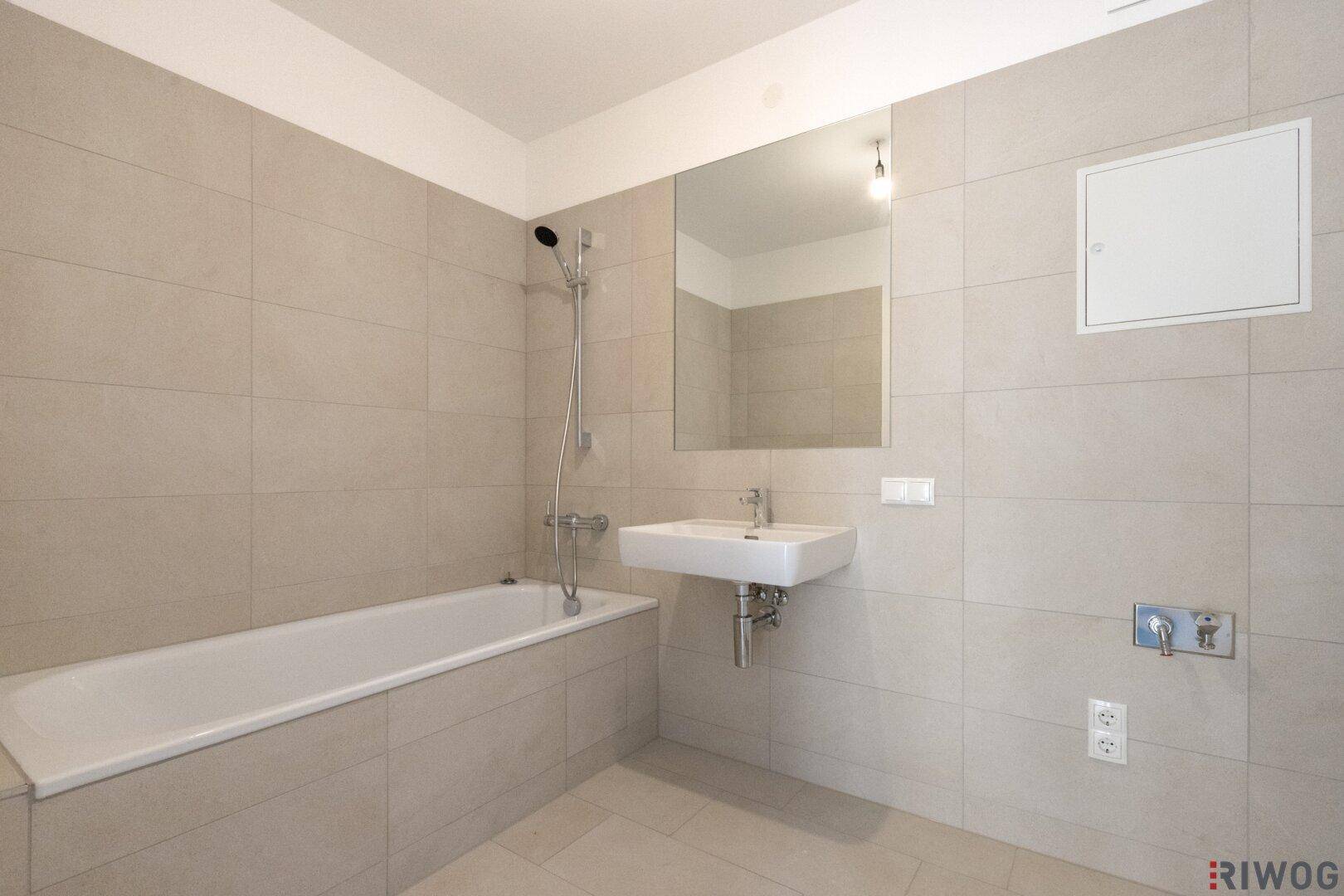 Modernes Badezimmer mit Badewanne, Waschbecken und hellen Fliesen an Wänden und Boden.
