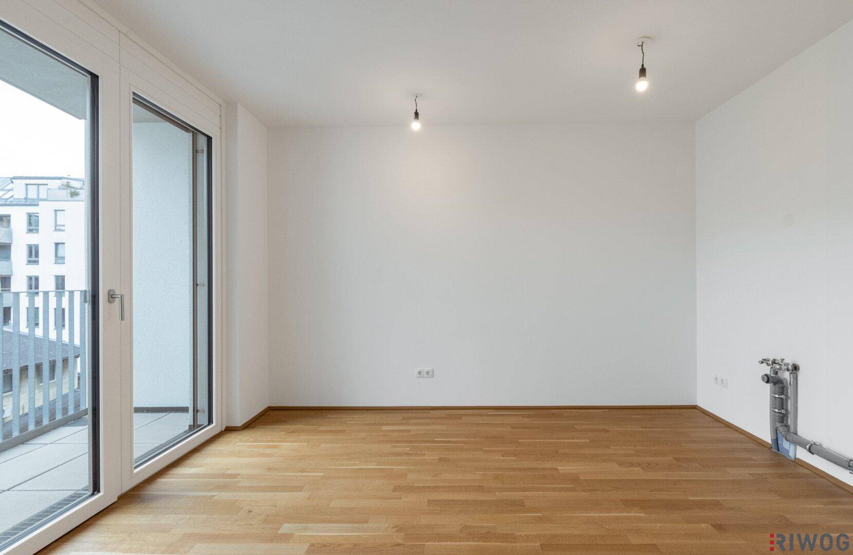 Geräumiges Wohnzimmer mit Parkettboden und Zugang zu einem Balkon.