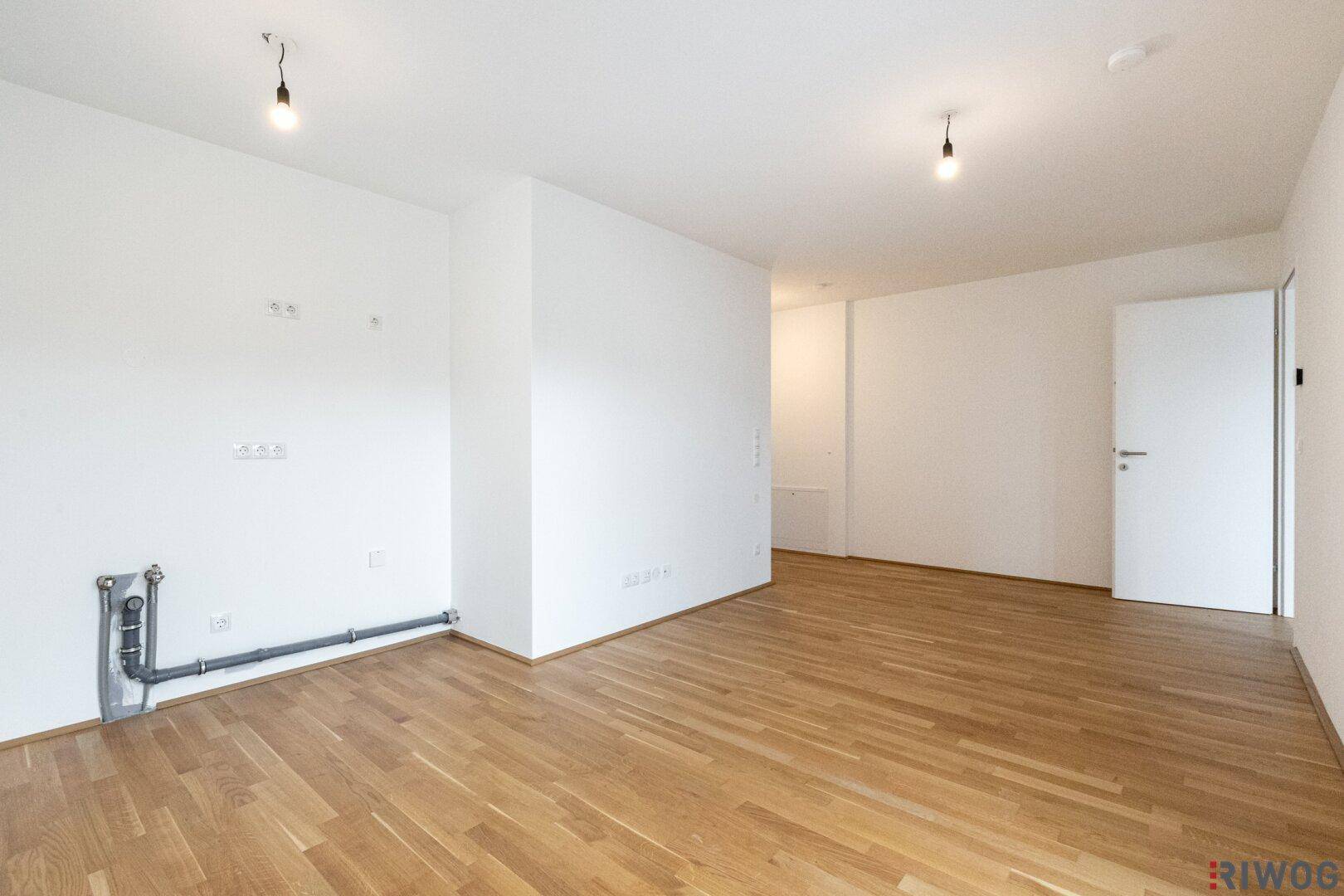 Leerer Wohnraum mit Parkettboden und weißen Wänden, ideal für individuelle Gestaltung.