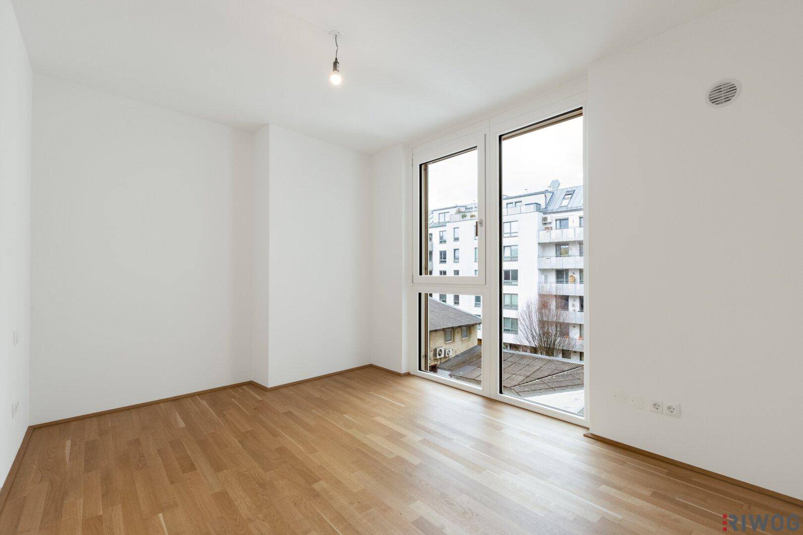 Helles Zimmer mit Parkettboden und großen Fenstern, ideal als Schlaf- oder Arbeitszimmer.