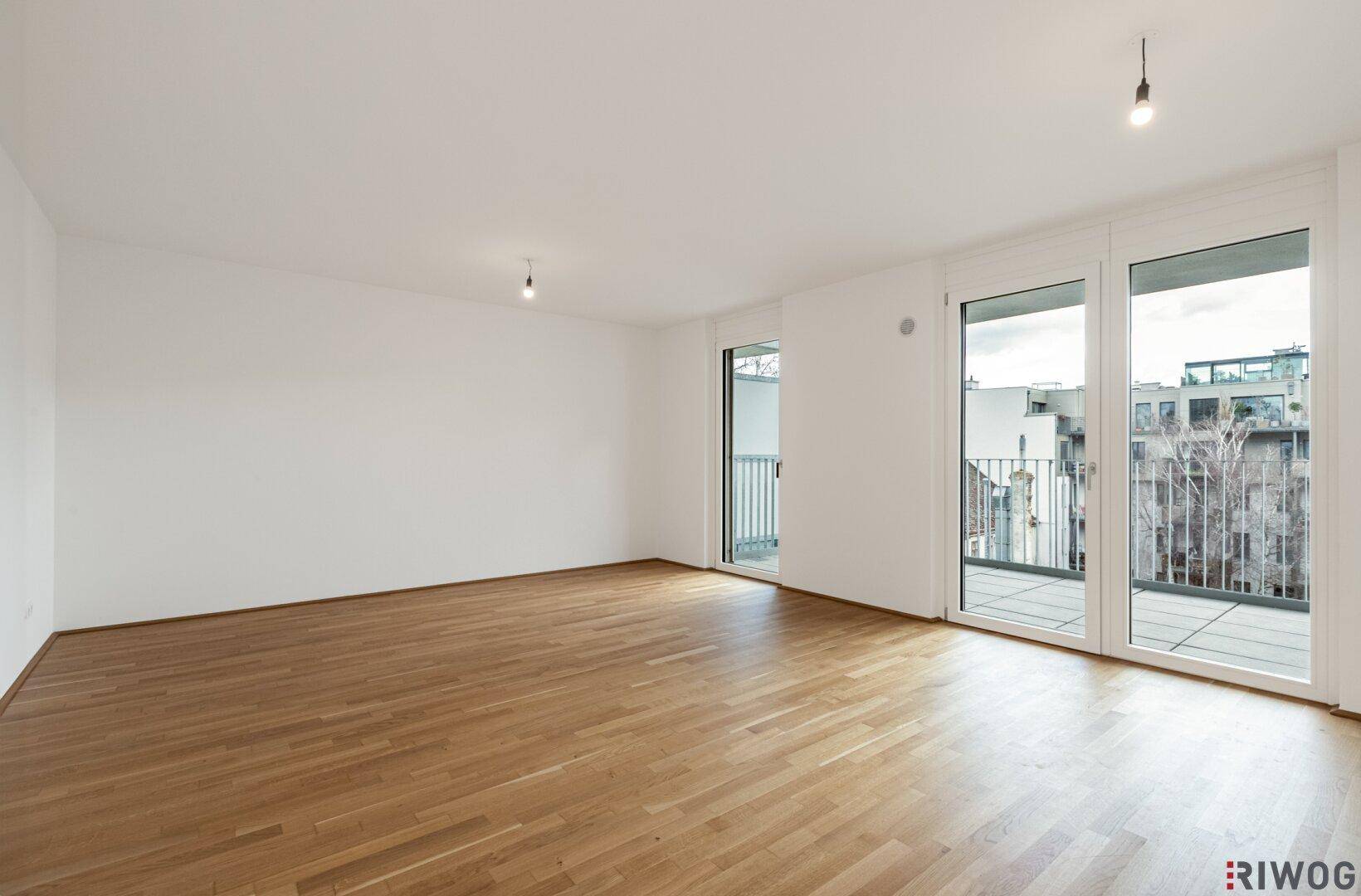 Geräumiges, leeres Wohnzimmer mit hellem Parkettboden und großen Fenstern, bereit zur individuellen Gestaltung.